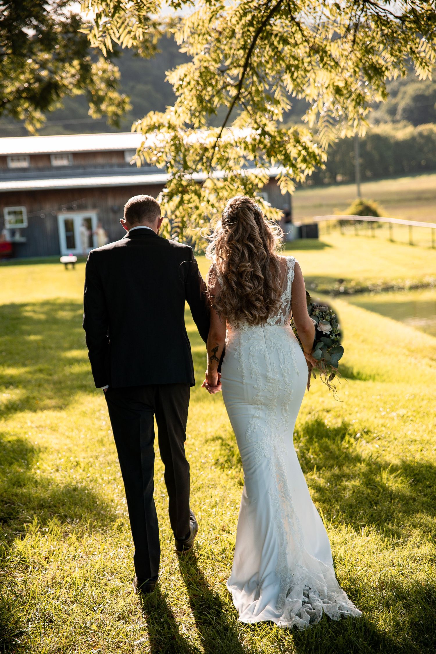 Bride and groom walking hand in hand across sunlit green lawn at outdoor wedding venue.