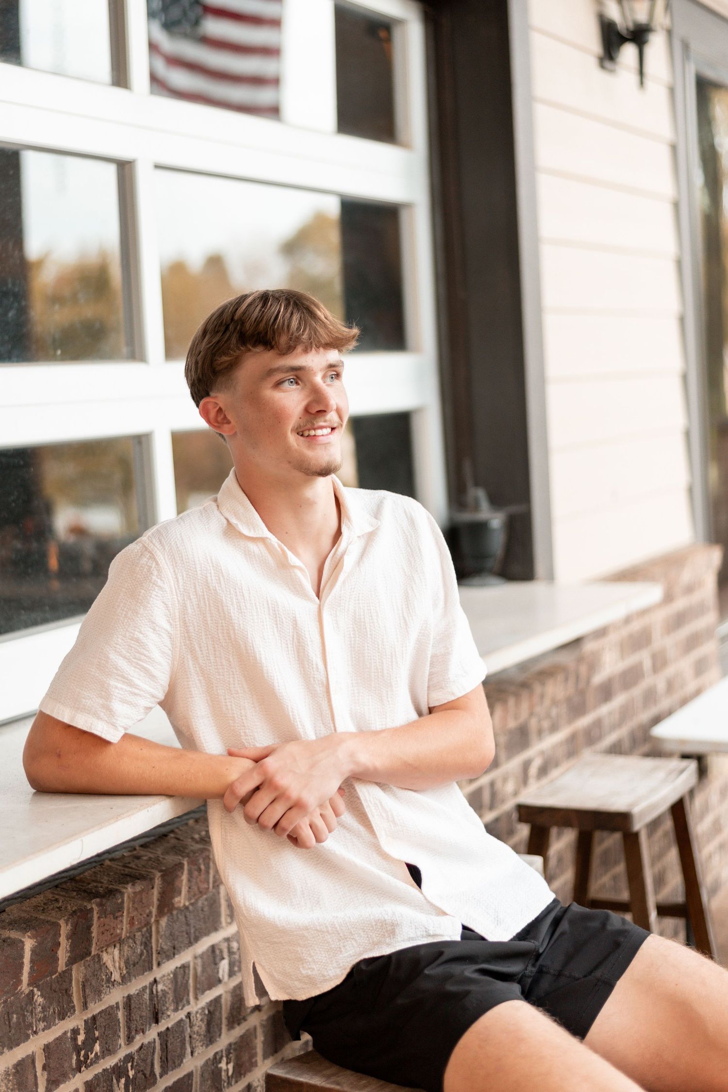 Person in white button-down shirt sits on brick ledge with American flag visible in background.
