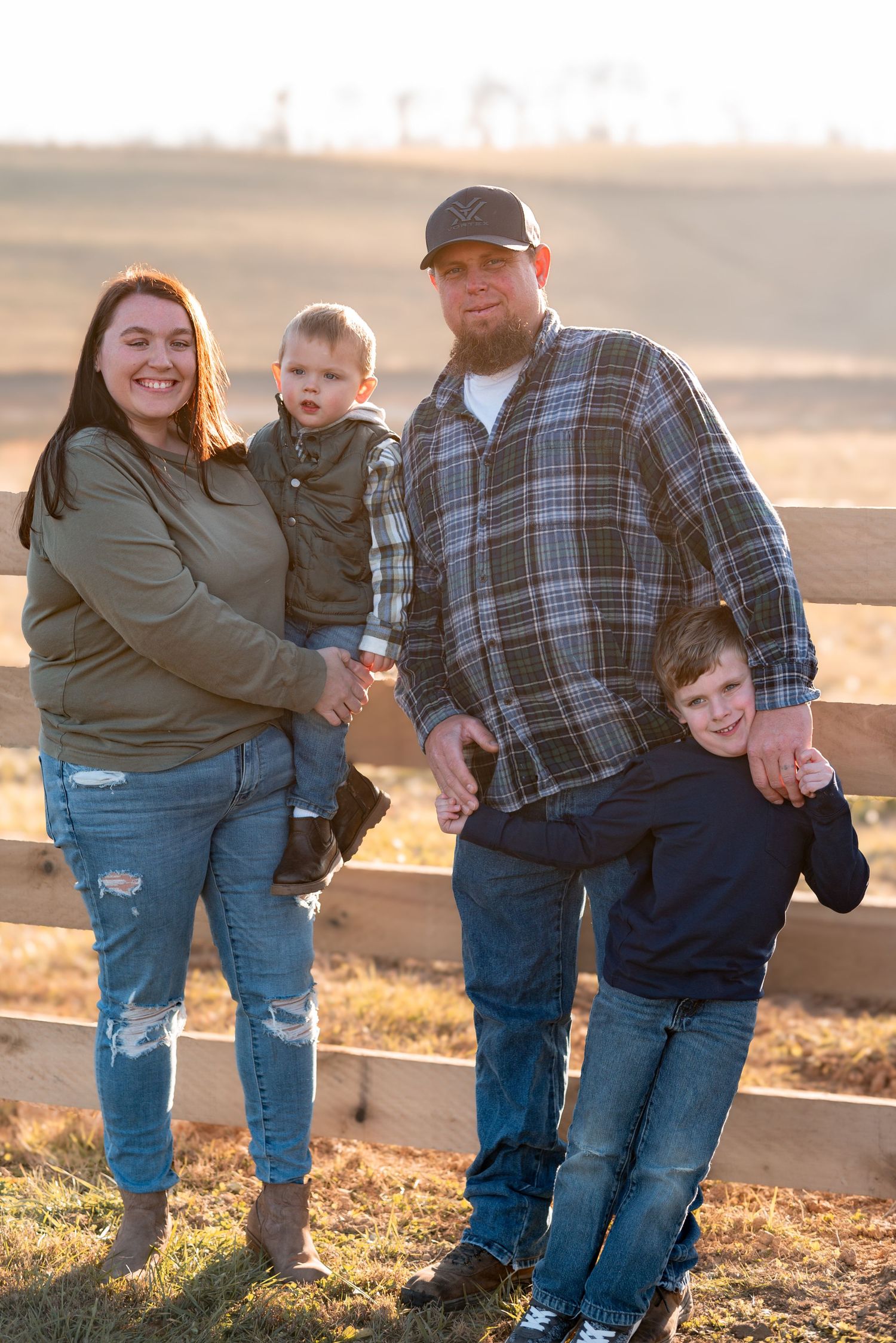 Warm sunset family photos taken by a wooden fence in casual denim outfits.
