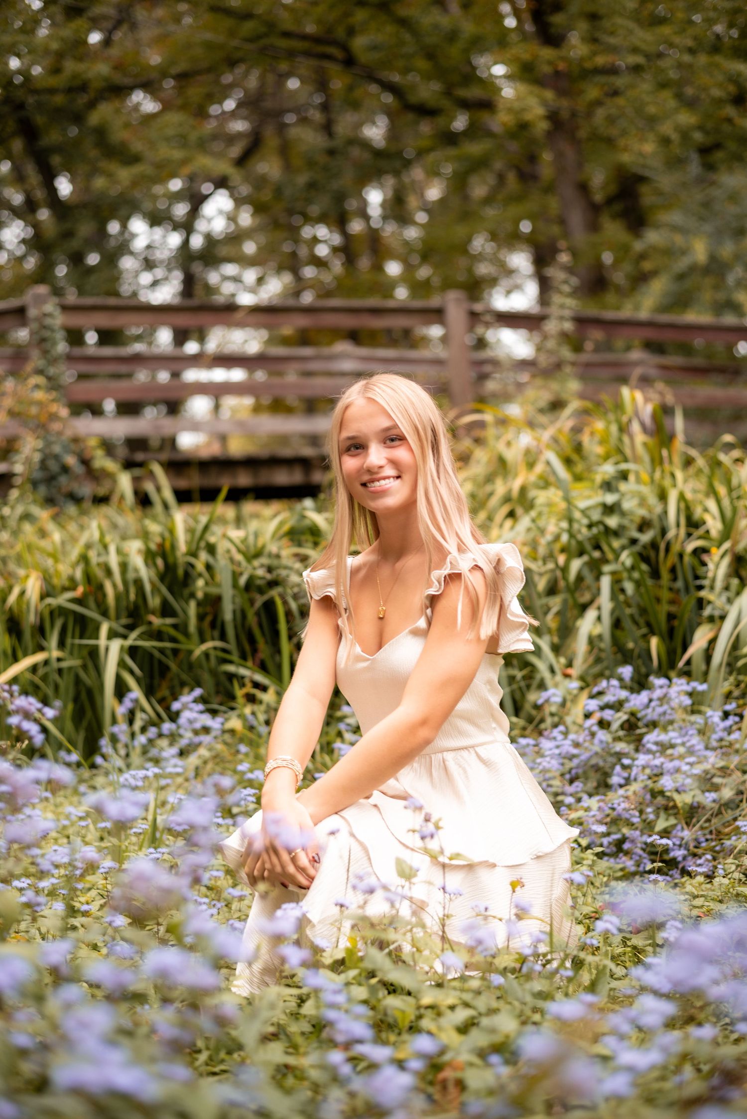 A white dress-clad figure sits among purple wildflowers in a garden setting during golden hour.