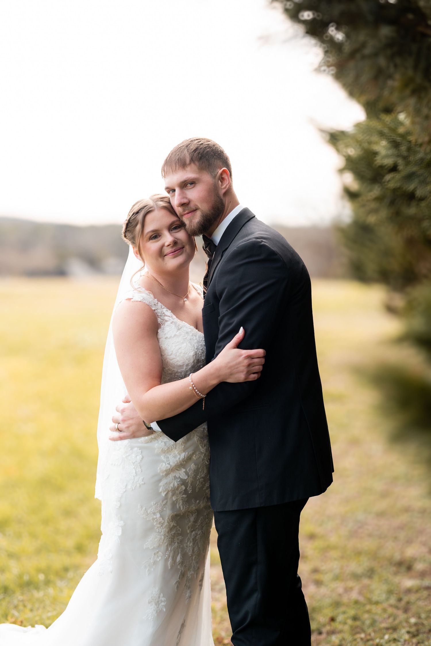 A tender moment between newlyweds in formal attire against a natural outdoor setting.