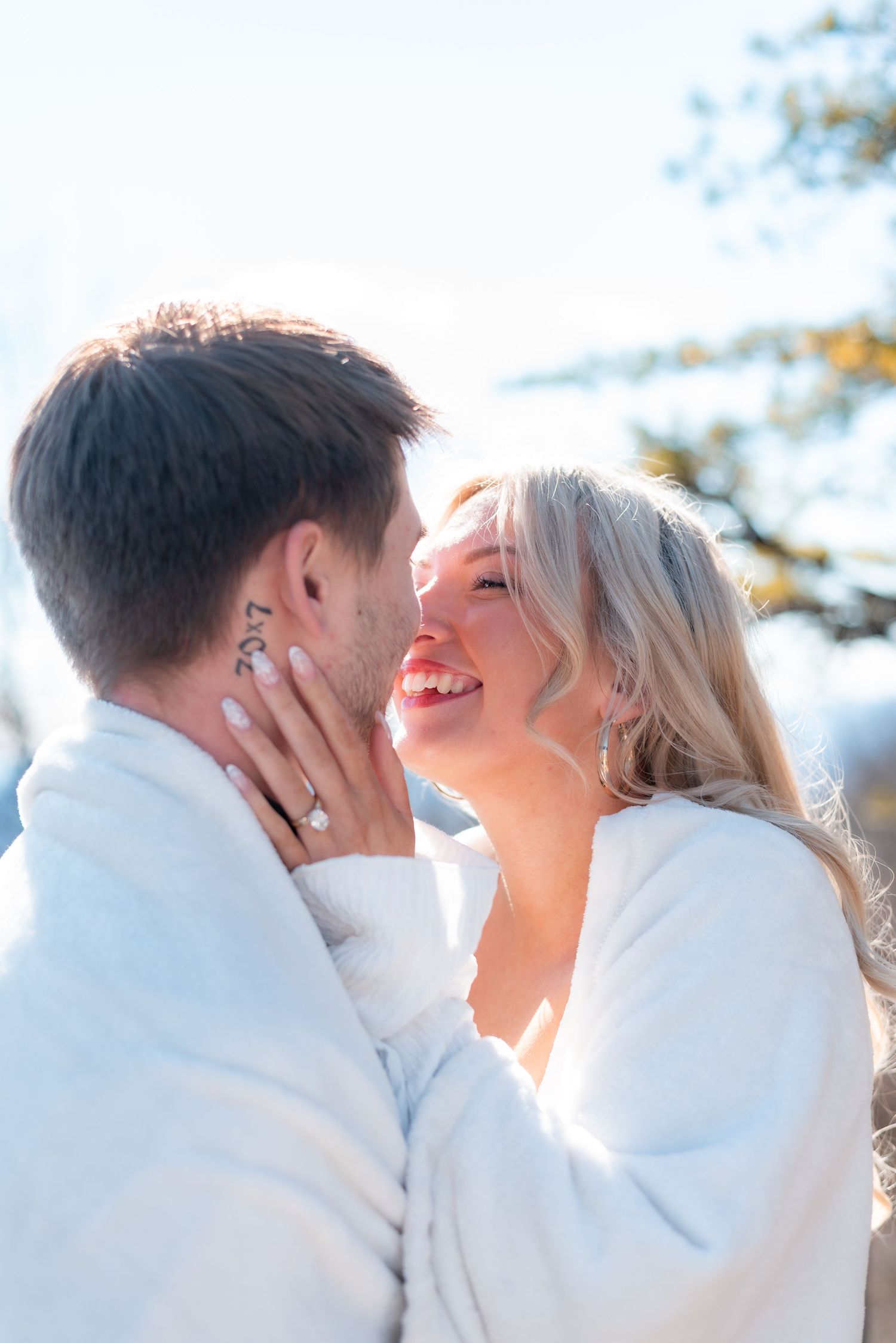 Romantic couple in white winter clothing embracing in soft sunlight.