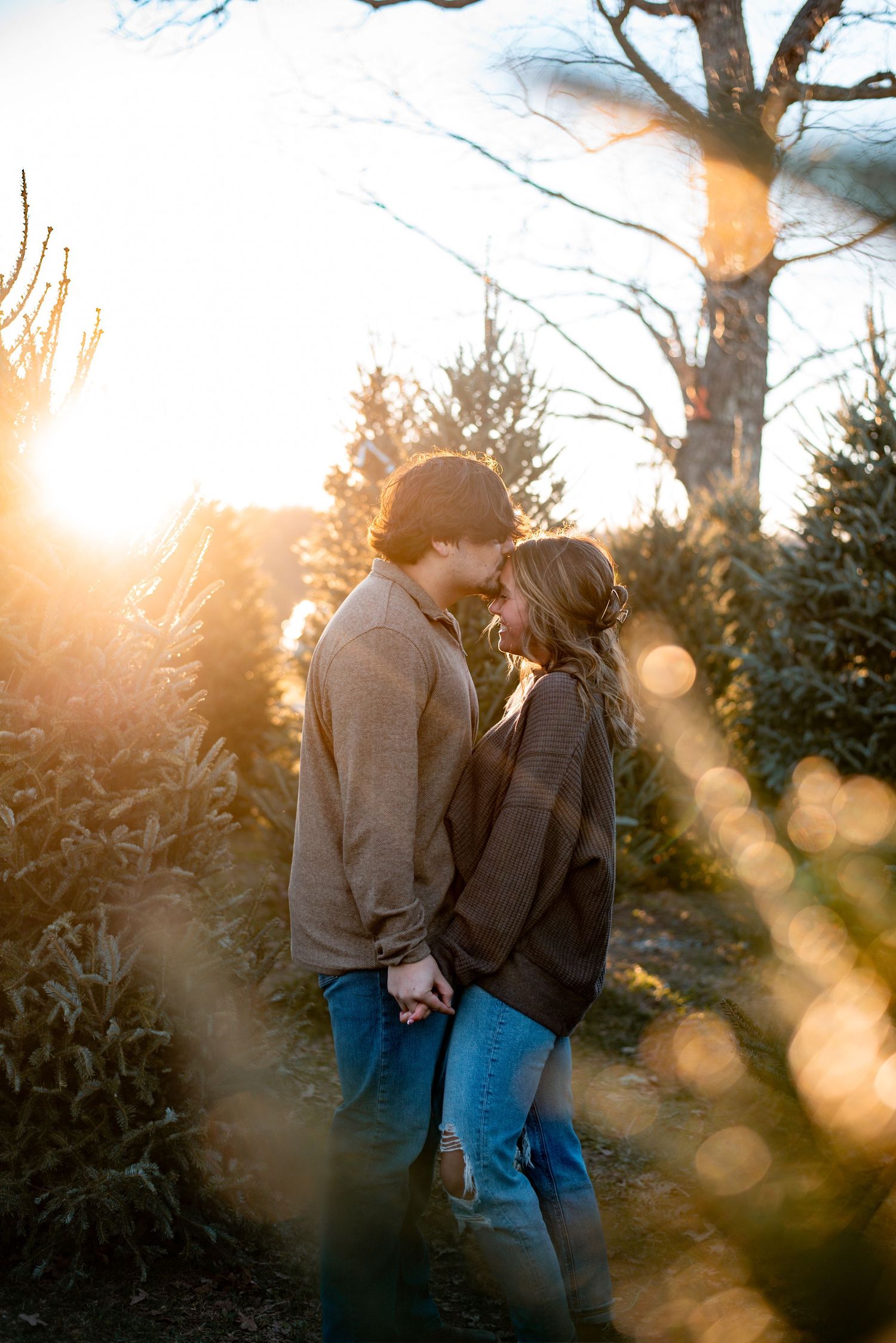 A romantic couple embraces in a sunlit forest setting during golden hour.