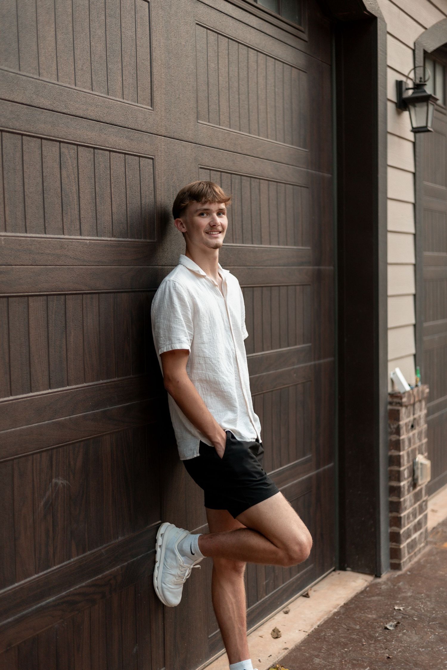 Person in white shirt poses against brown garage door during casual photo shoot.