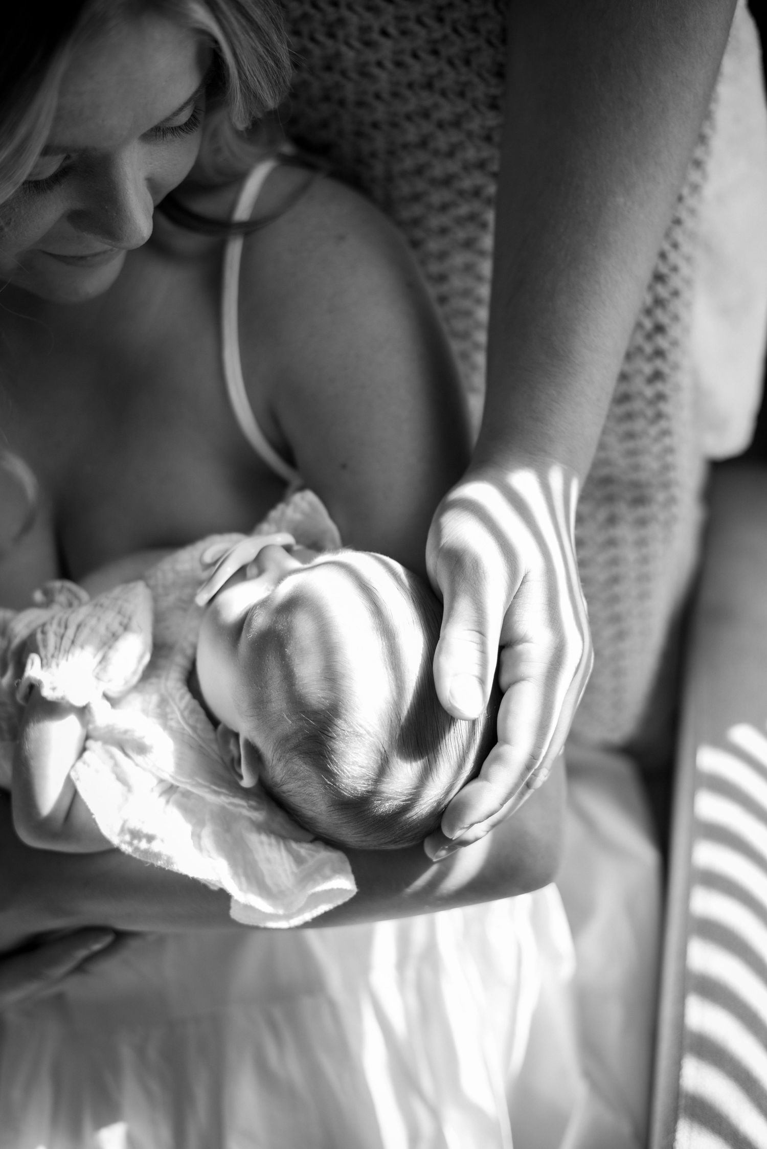 Black and white close-up of gentle hands holding newborn in natural light.