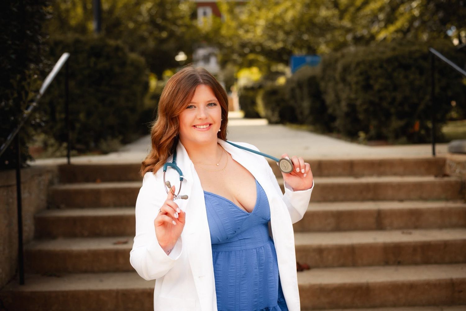 Healthcare professional in white coat and blue dress on stone steps.