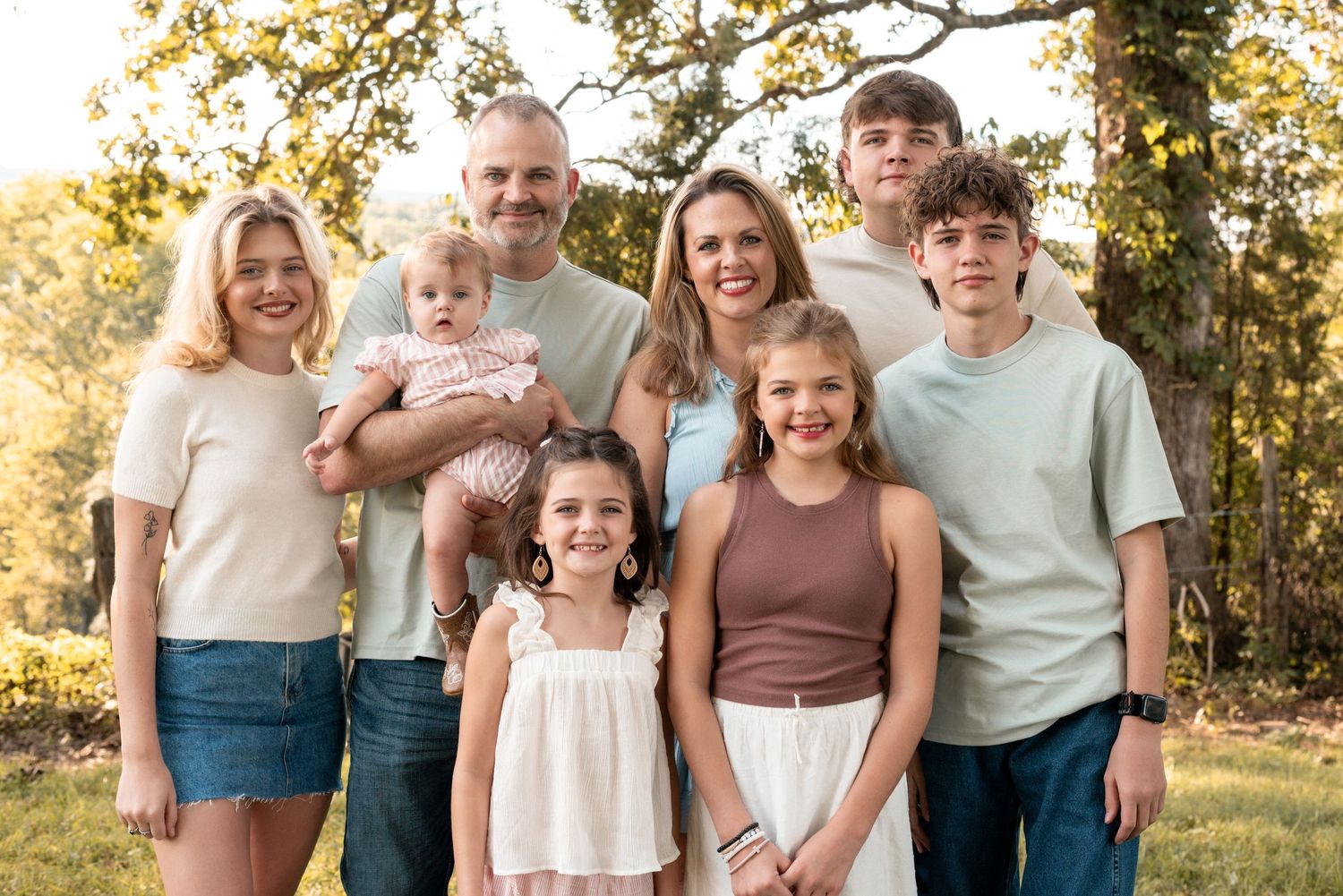 Extended family gathers for outdoor portrait session in casual coordinating outfits.