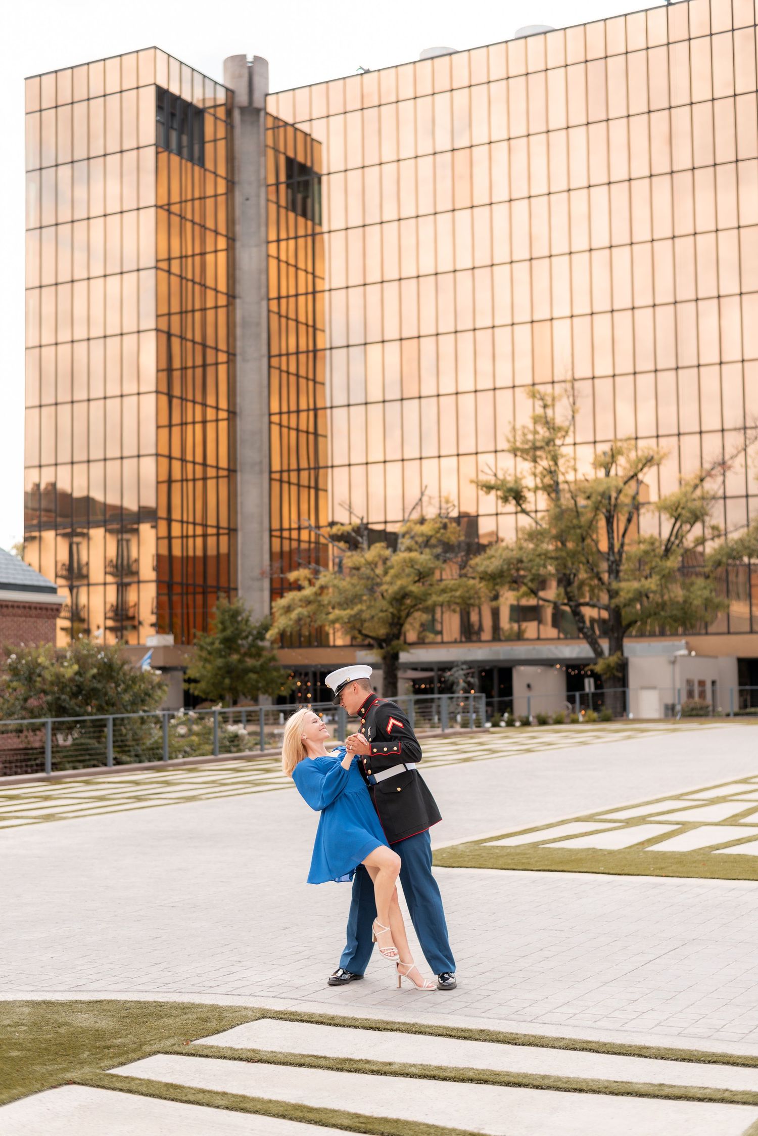 A couple poses together near a modern glass building with geometric architecture.