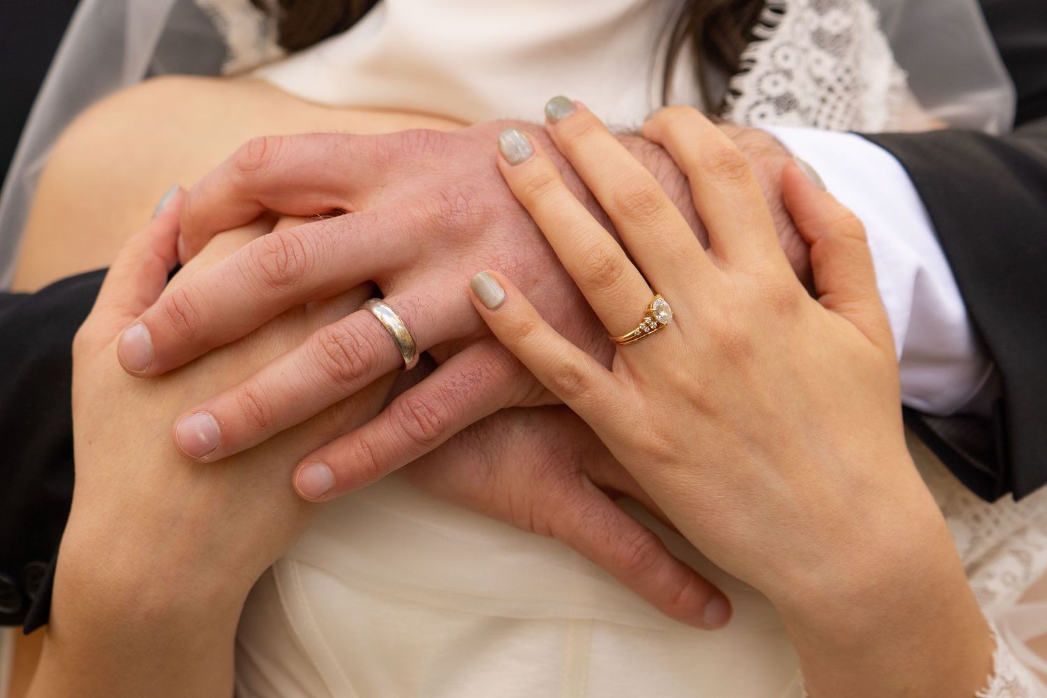 Close-up of newlyweds hands showing wedding rings, bride and groom embracing on their wedding day.