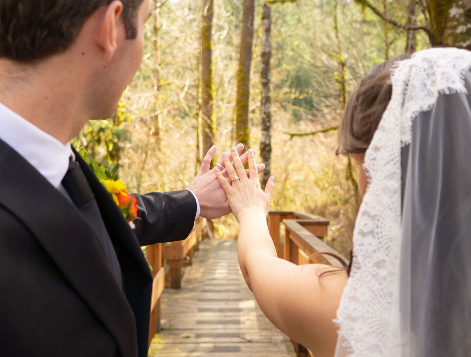 Groom places wedding ring on brides finger on a wooden bridge in autumn forest.