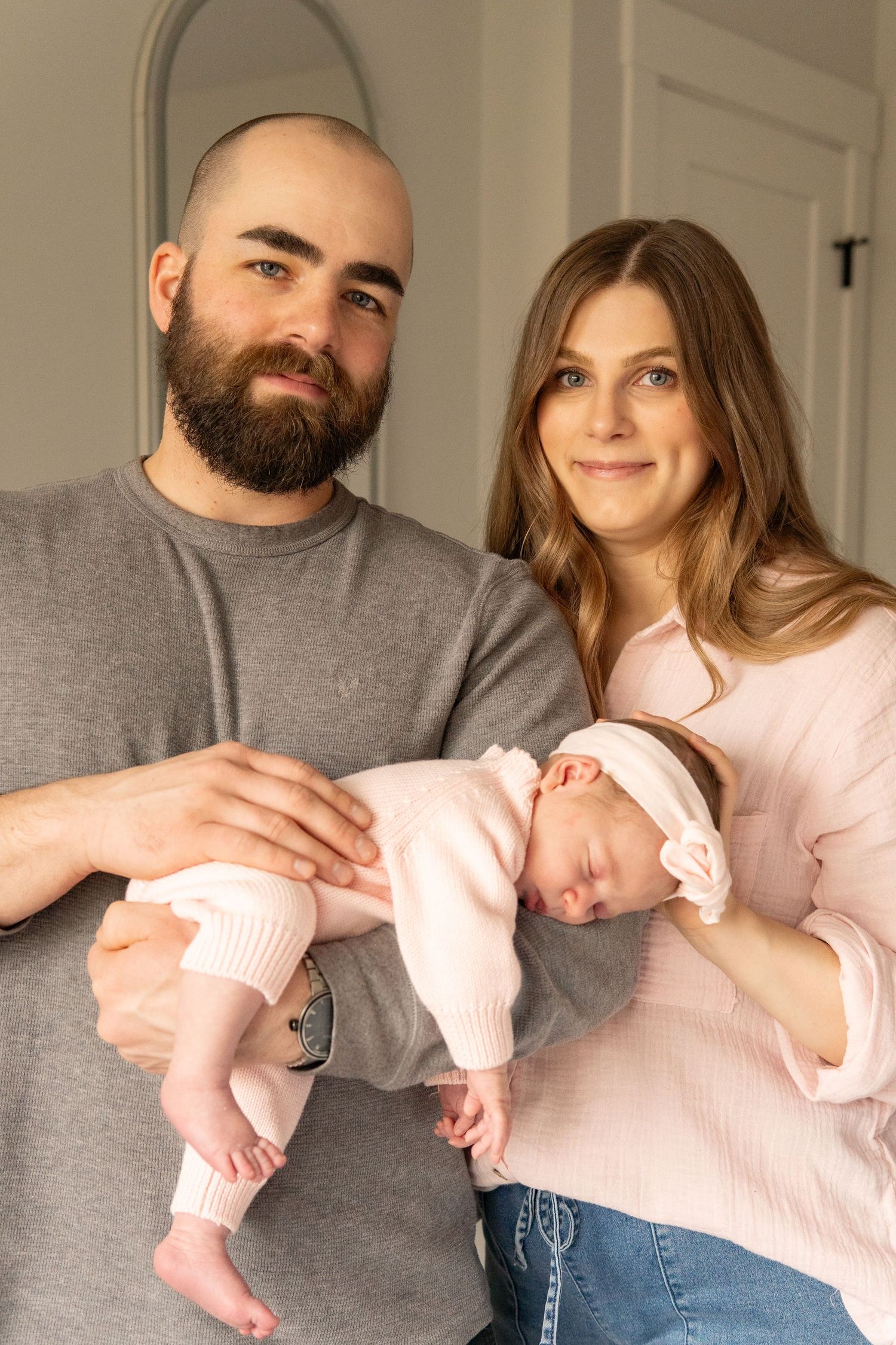 Happy new parents holding their sleeping newborn baby dressed in pink, posing together for a family portrait.