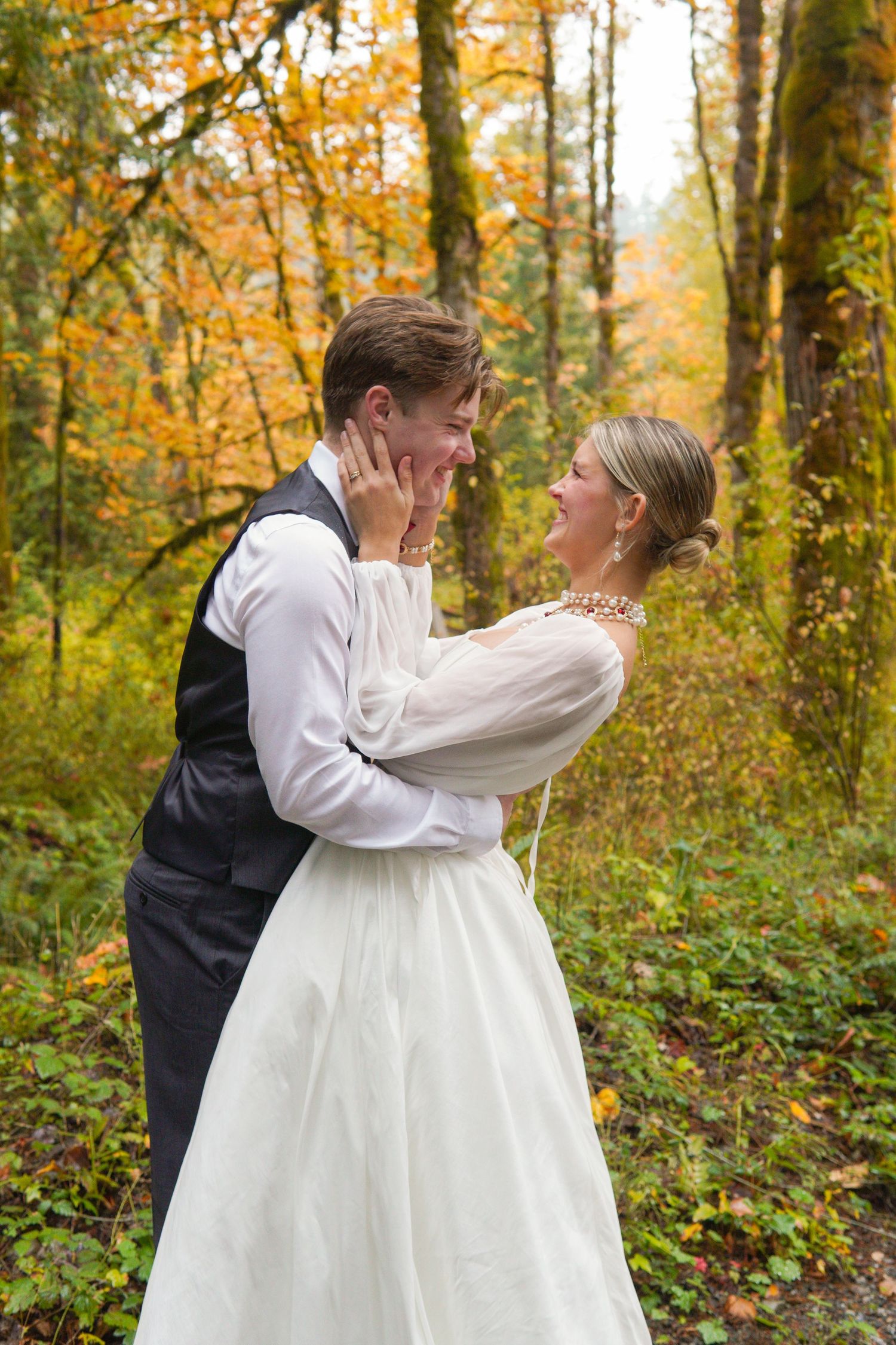 Bride and groom sharing a joyful moment surrounded by golden autumn foliage in the forest.