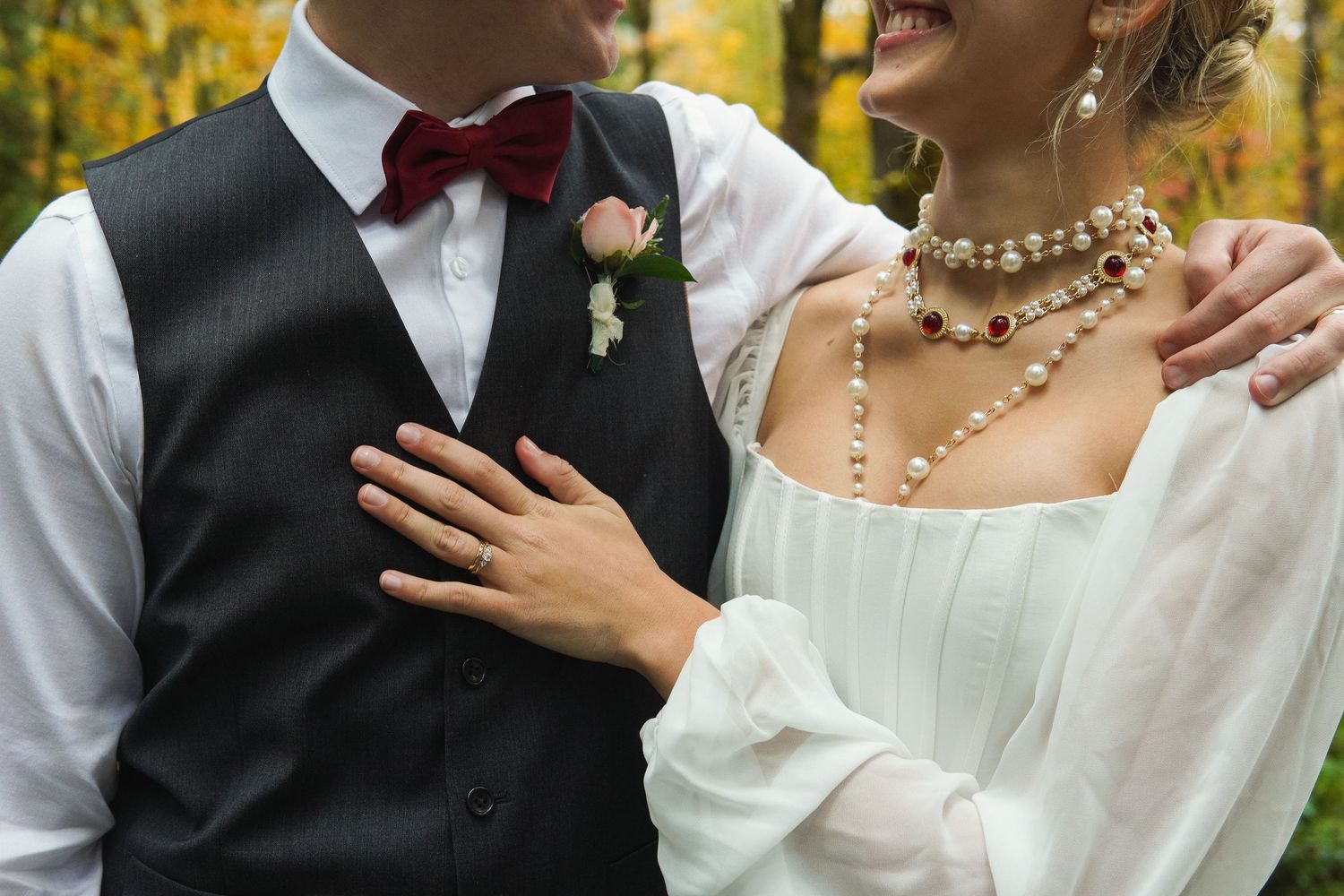 Bride in white dress with pearl necklace and groom in black vest with red bow tie.