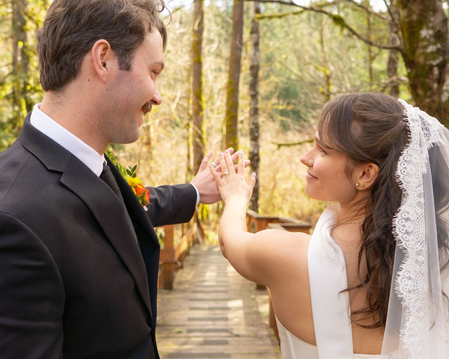 Bride and groom exchanging rings outdoors on a wooden bridge surrounded by lush forest trees.