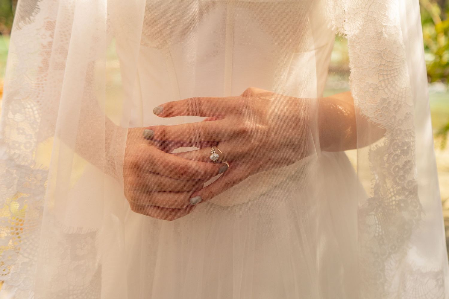 Close-up of bride's hand displaying a diamond engagement ring over her white wedding gown.