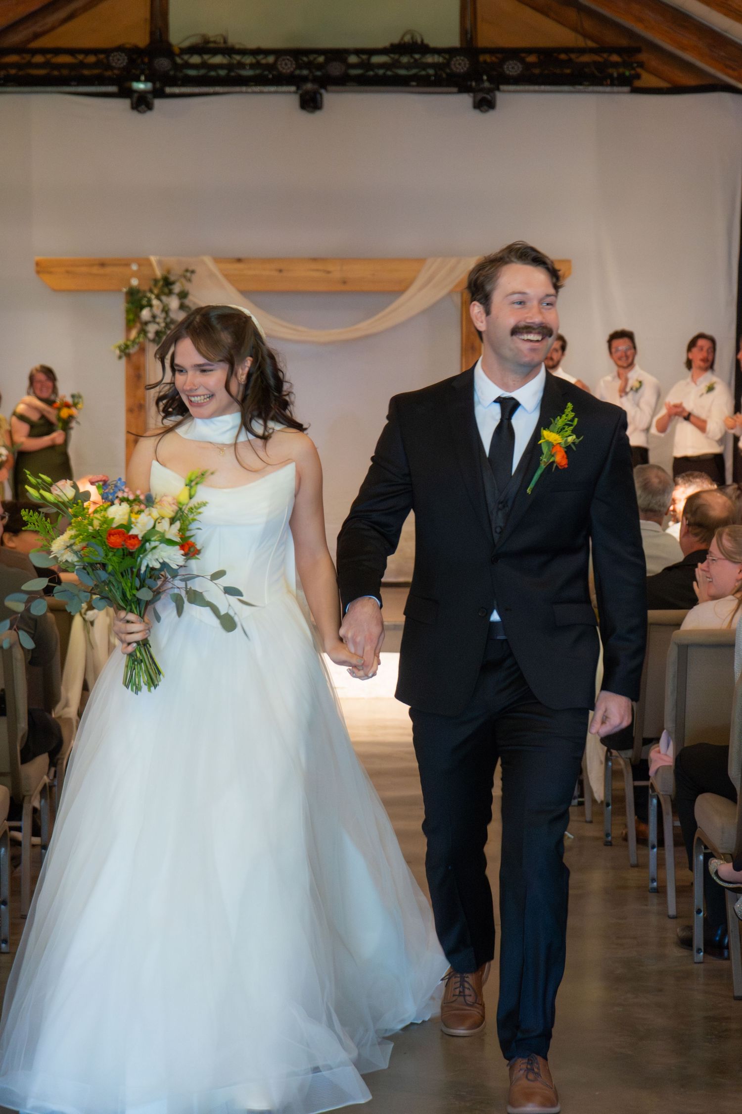 Newlywed couple holding hands walking back down the aisle after wedding ceremony in a rustic venue.