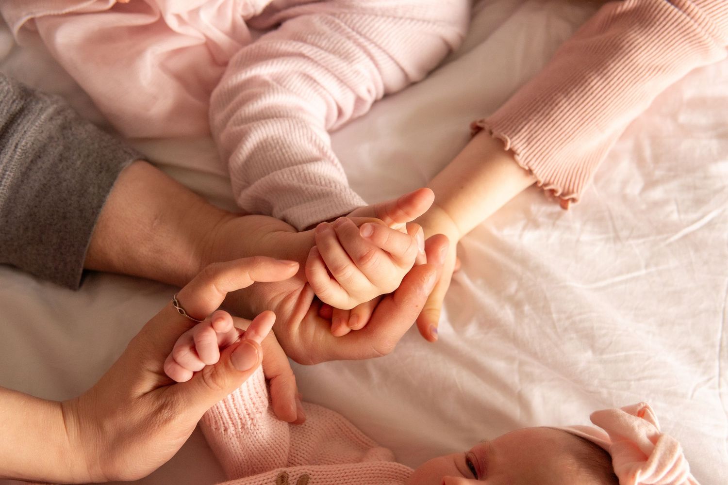 Family hands holding together on a soft pink bed, symbolizing love and unity between parents and newborn baby.