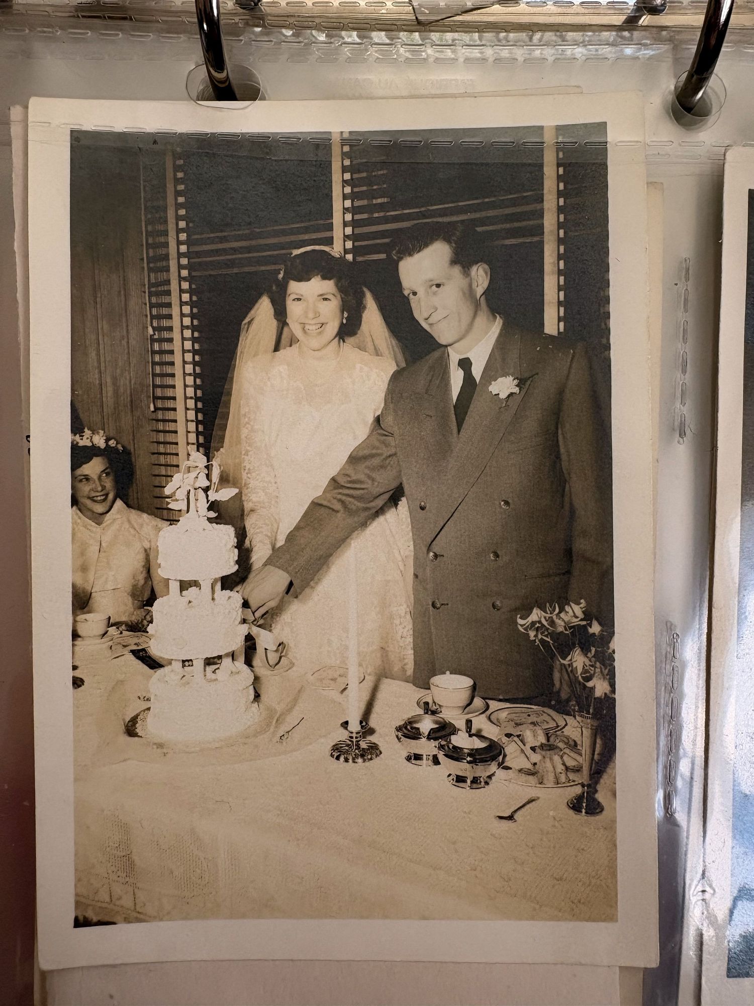 Vintage black and white wedding photo of couple cutting cake, bride in veil and groom in suit, 1950s era.