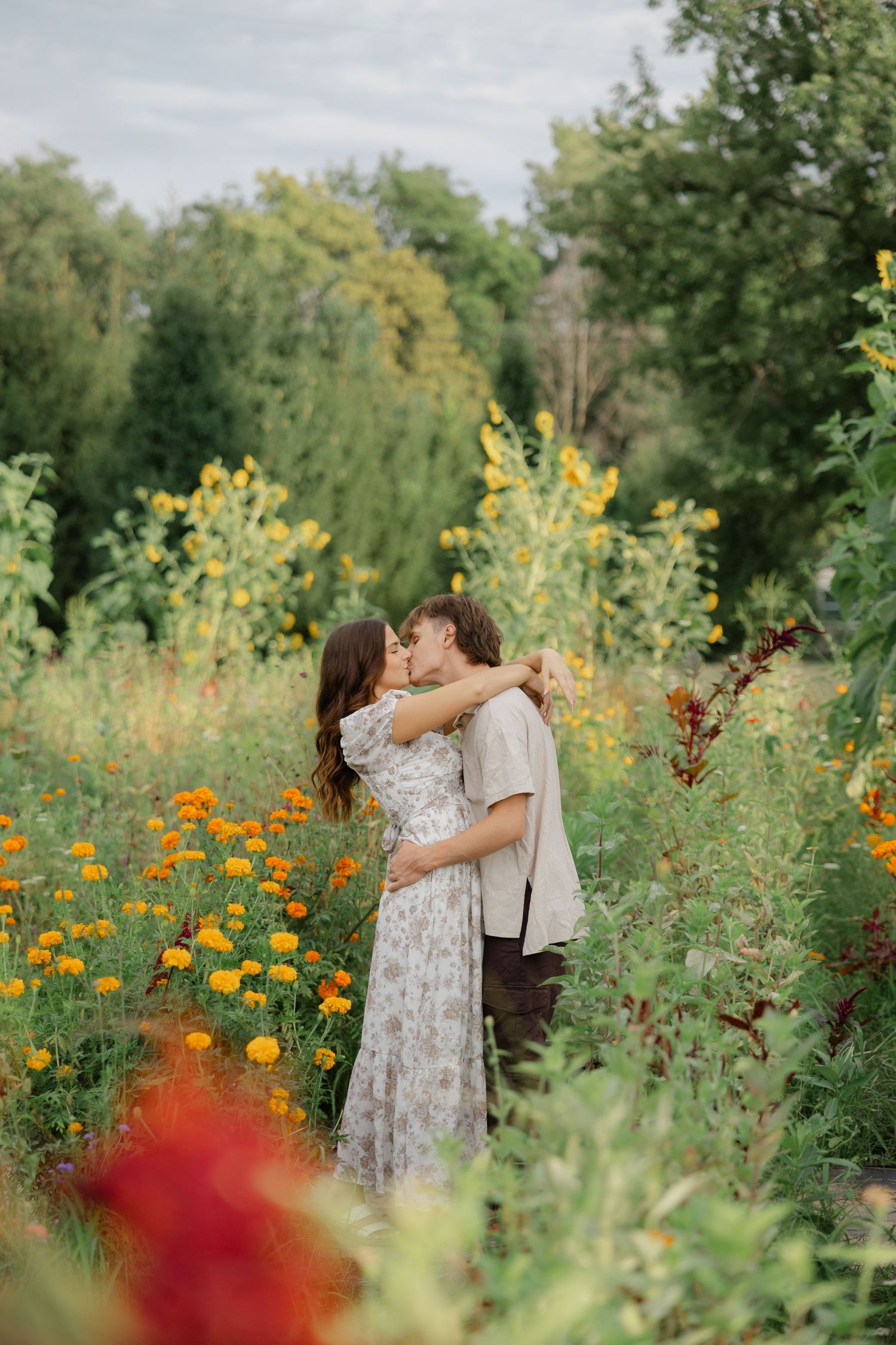 A romantic moment captured in a vibrant garden filled with orange and yellow flowers on a sunny summer day.