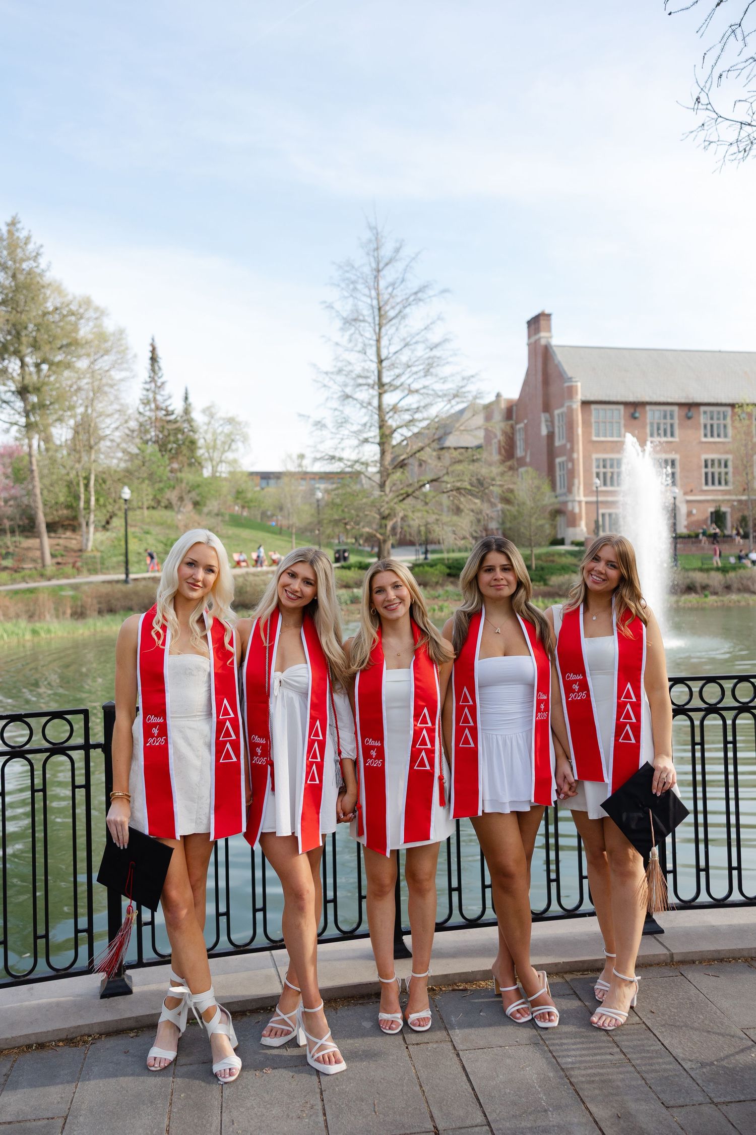 A group wearing matching red and white outfits poses together on a bridge railing near a pond. Ohio state grad photos