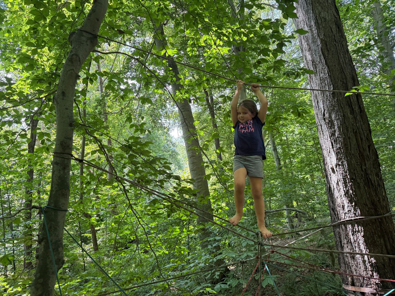 Child hangs from a rope between trees in a dense green forest.
