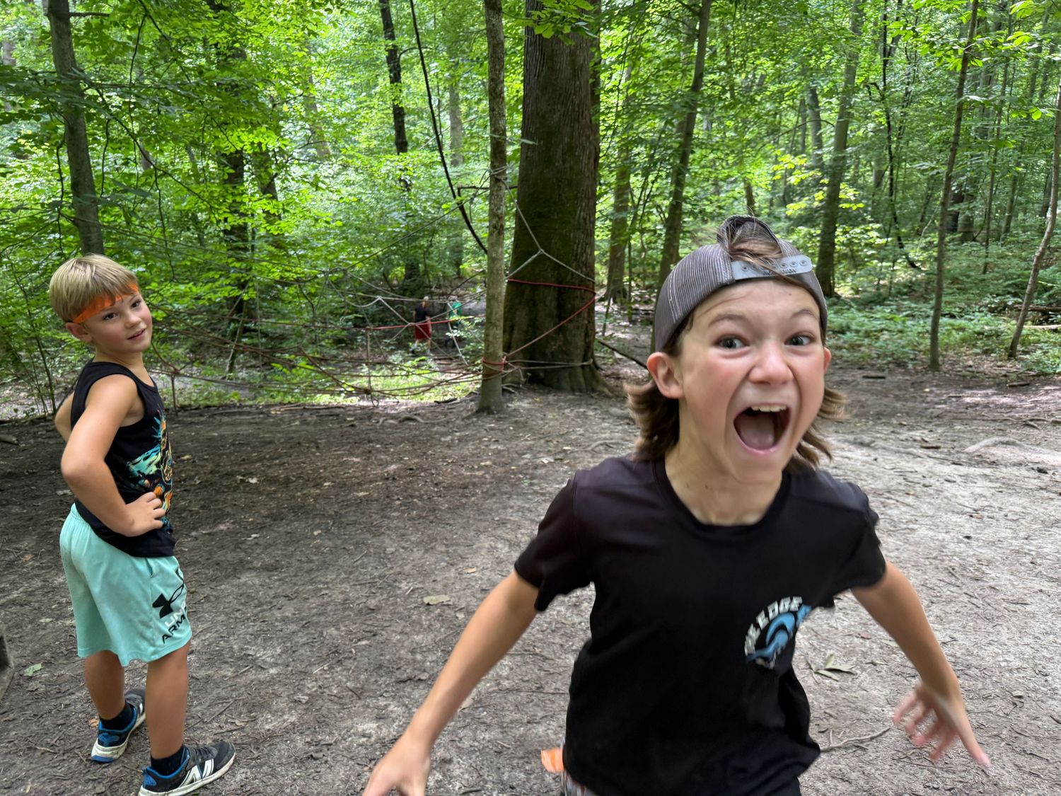 Energetic boy makes a funny face running toward camera in a green forest setting.
