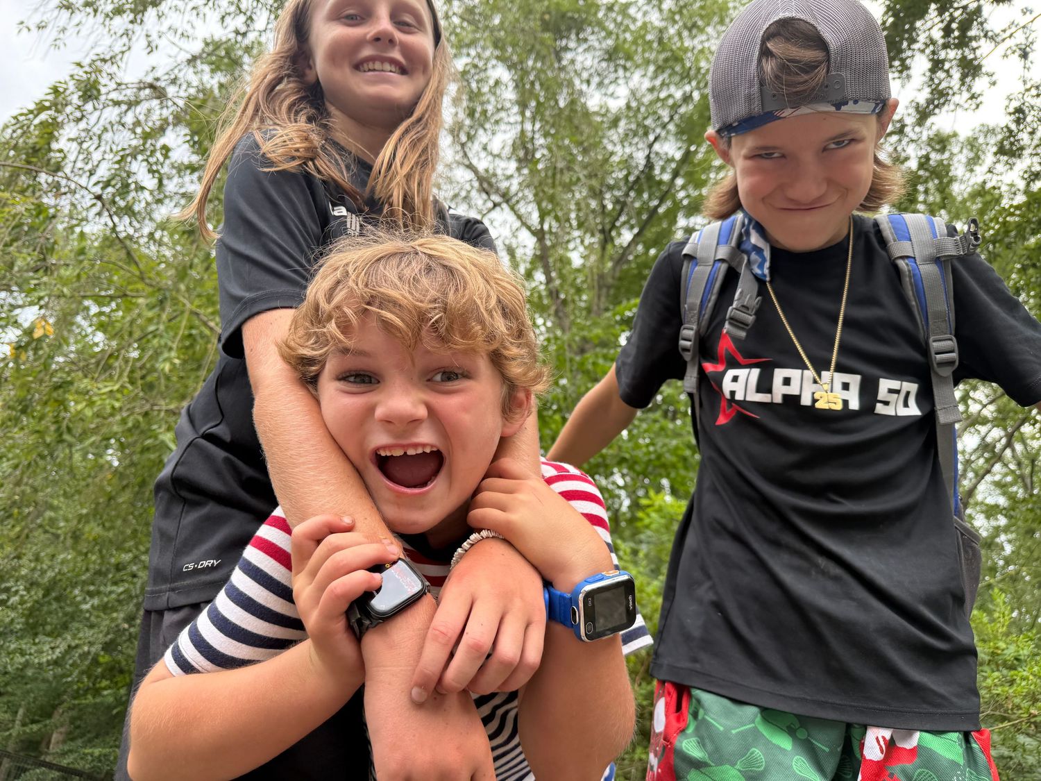 Three happy kids laughing and playing together outdoors at summer camp in the woods.