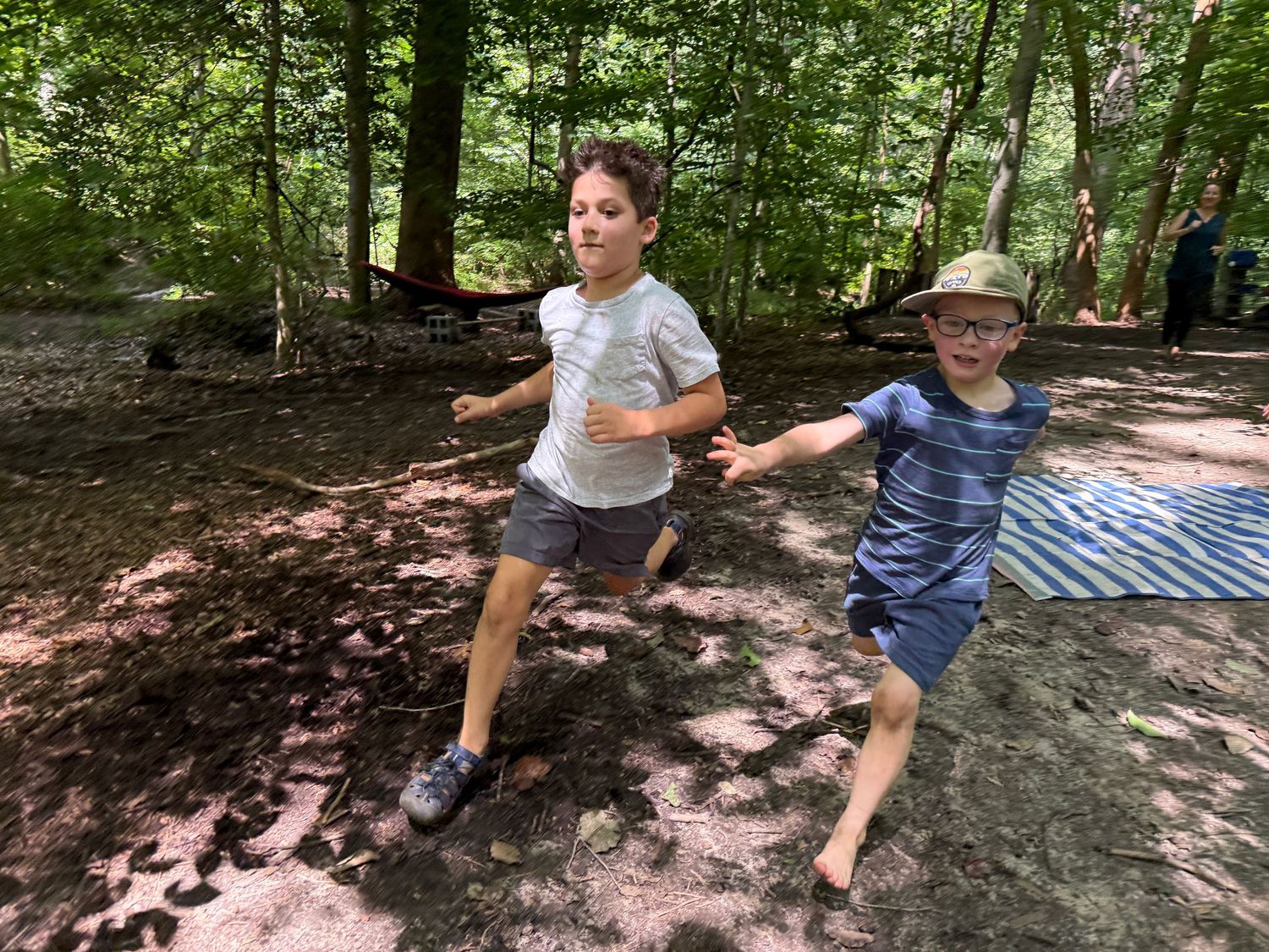 Two children running and playing together in a shaded forest clearing outdoors.