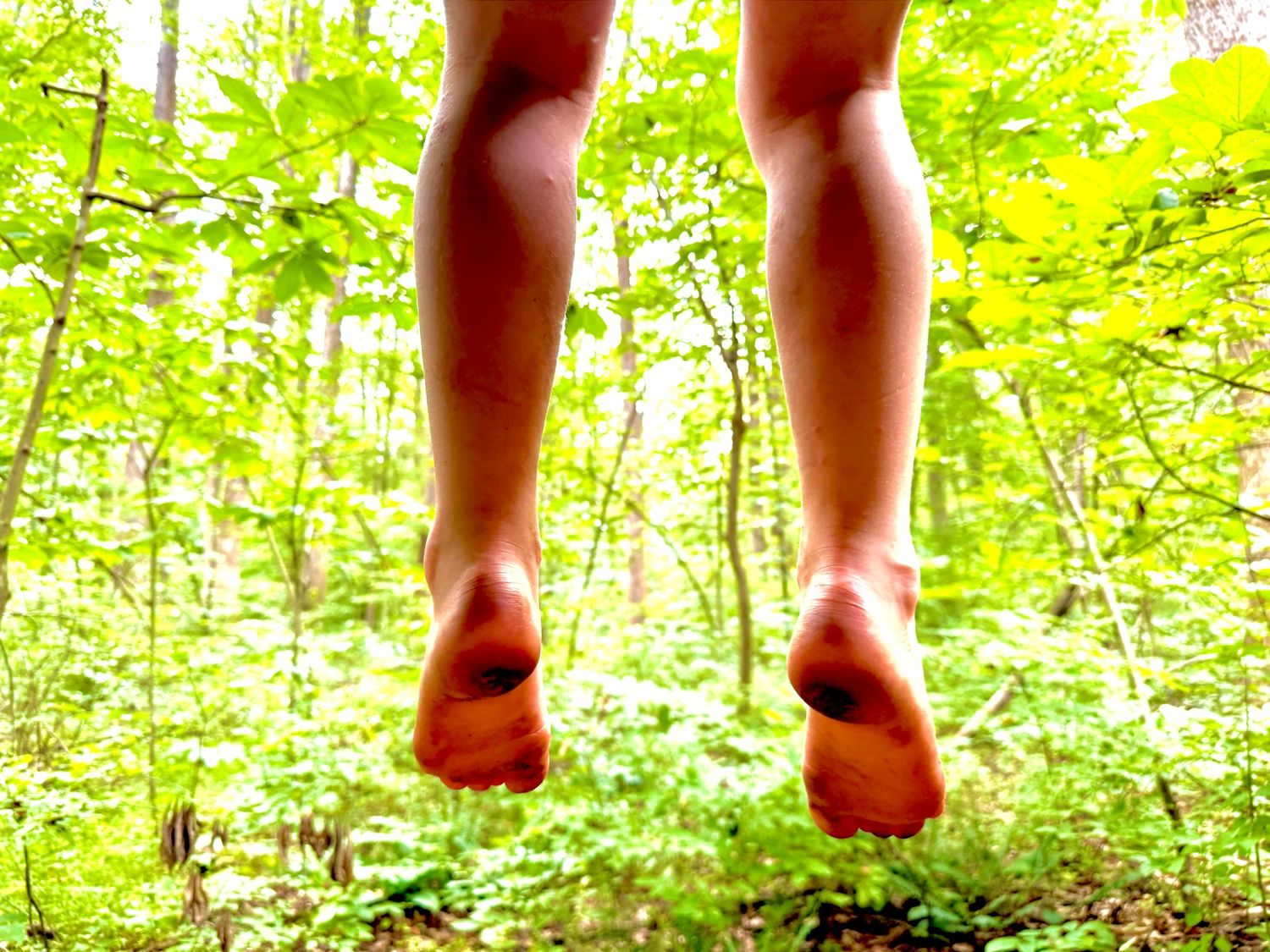 Barefoot child jumping in a lush green forest, captured from ground level perspective.