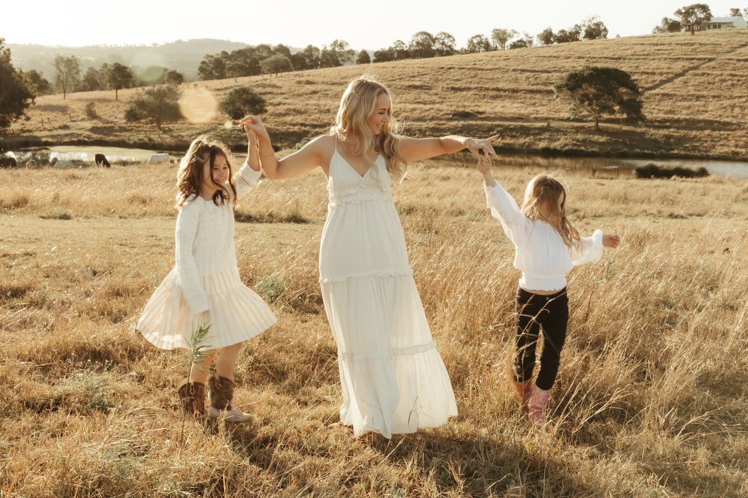 Mum twirling her daughters in a golden paddock at sunset, captured during a heartfelt Ipswich family session.