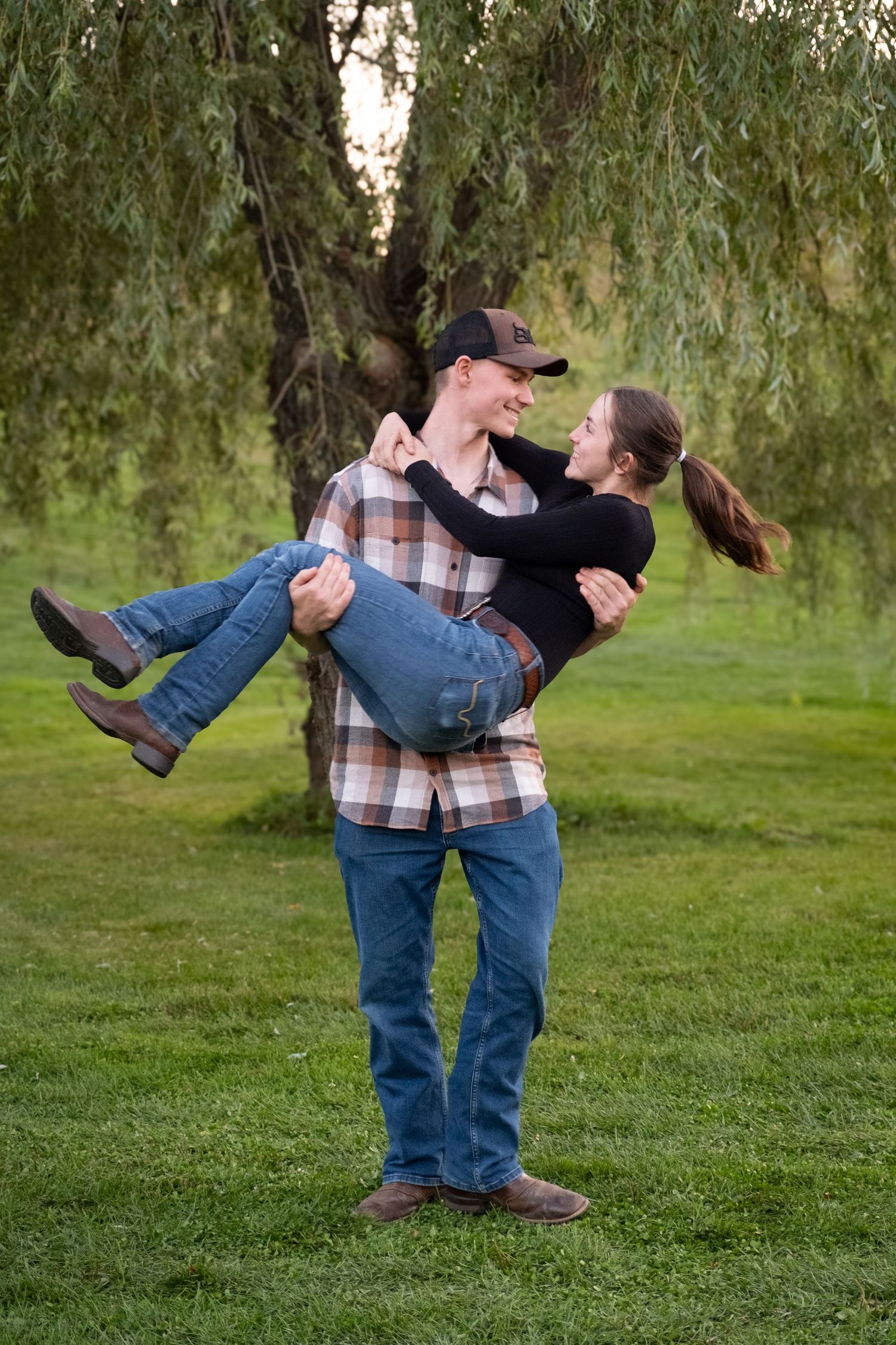Playful couple sharing a tender moment under a willow tree.