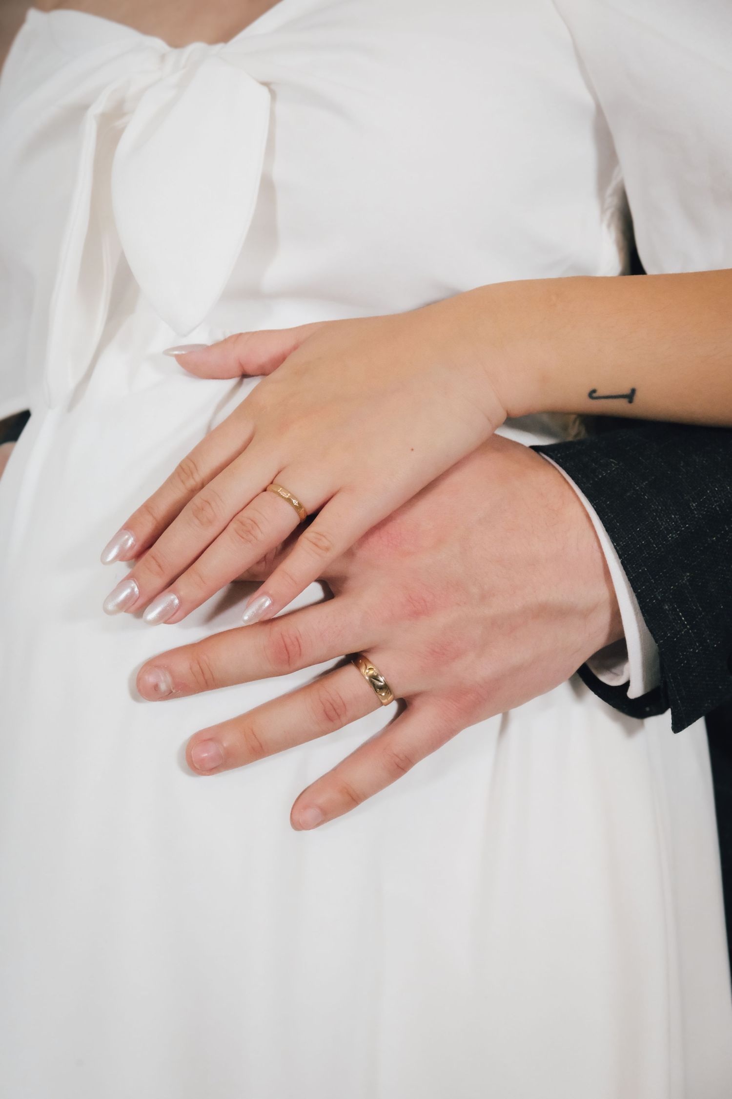 Close-up of wedding rings on bride and groom's hands against white dress fabric.