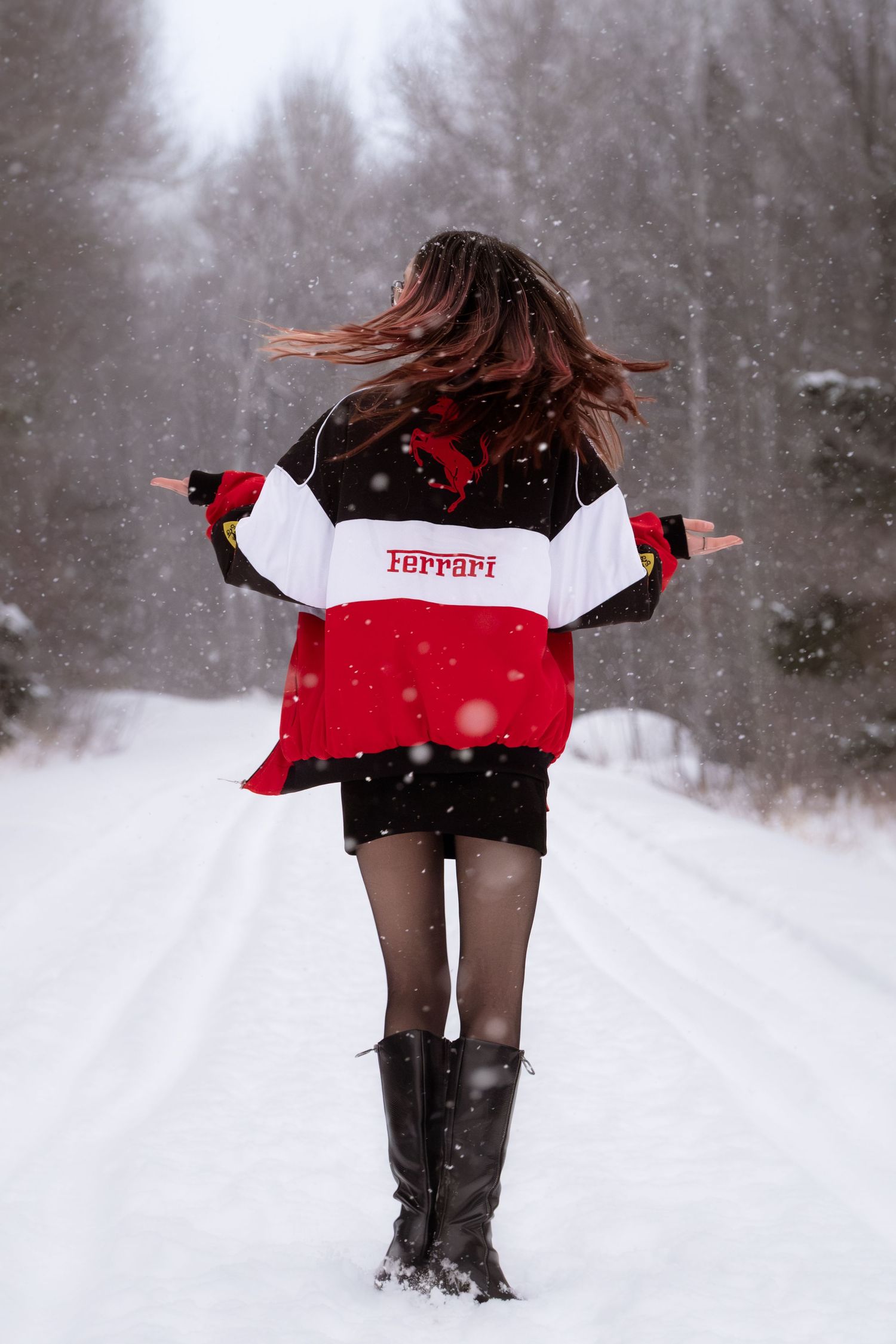 A person wearing red and white clothing twirls playfully in the falling snow on a winter day.