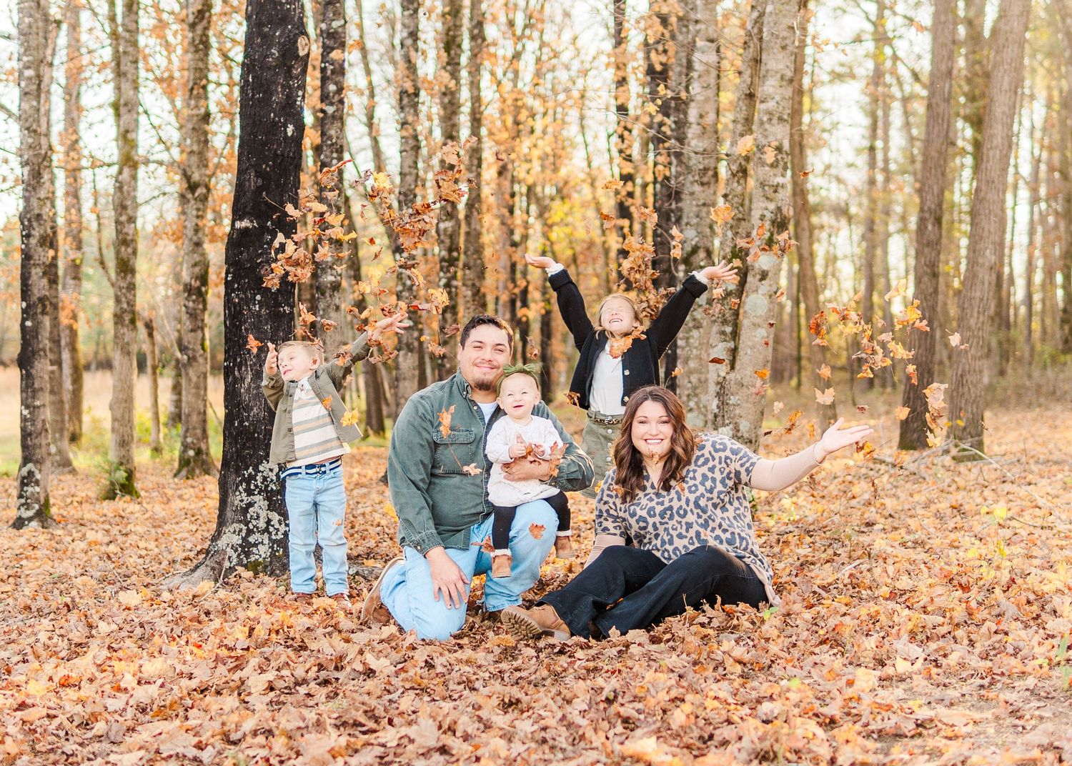 A group sits together in a wooded area covered with fallen autumn leaves during golden hour.