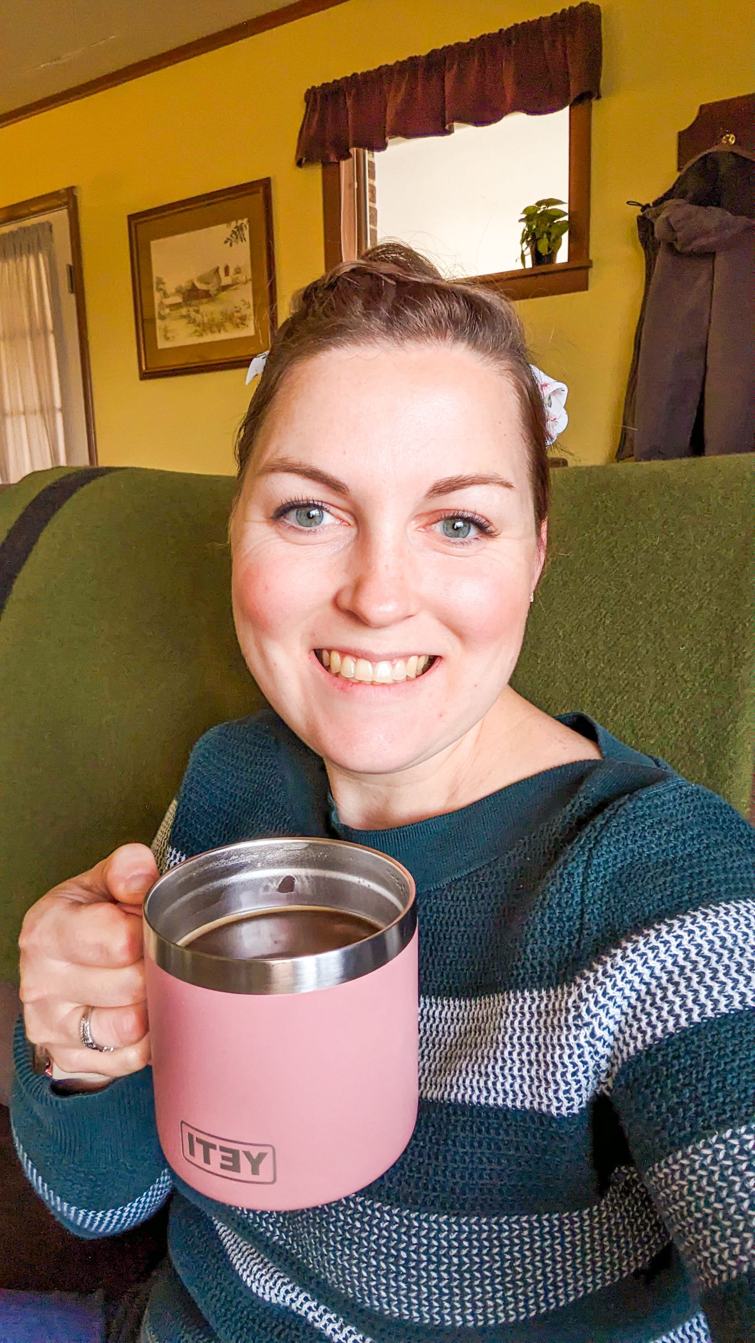 Someone relaxes in a green armchair holding a pink YETI tumbler while wearing a striped teal sweater.