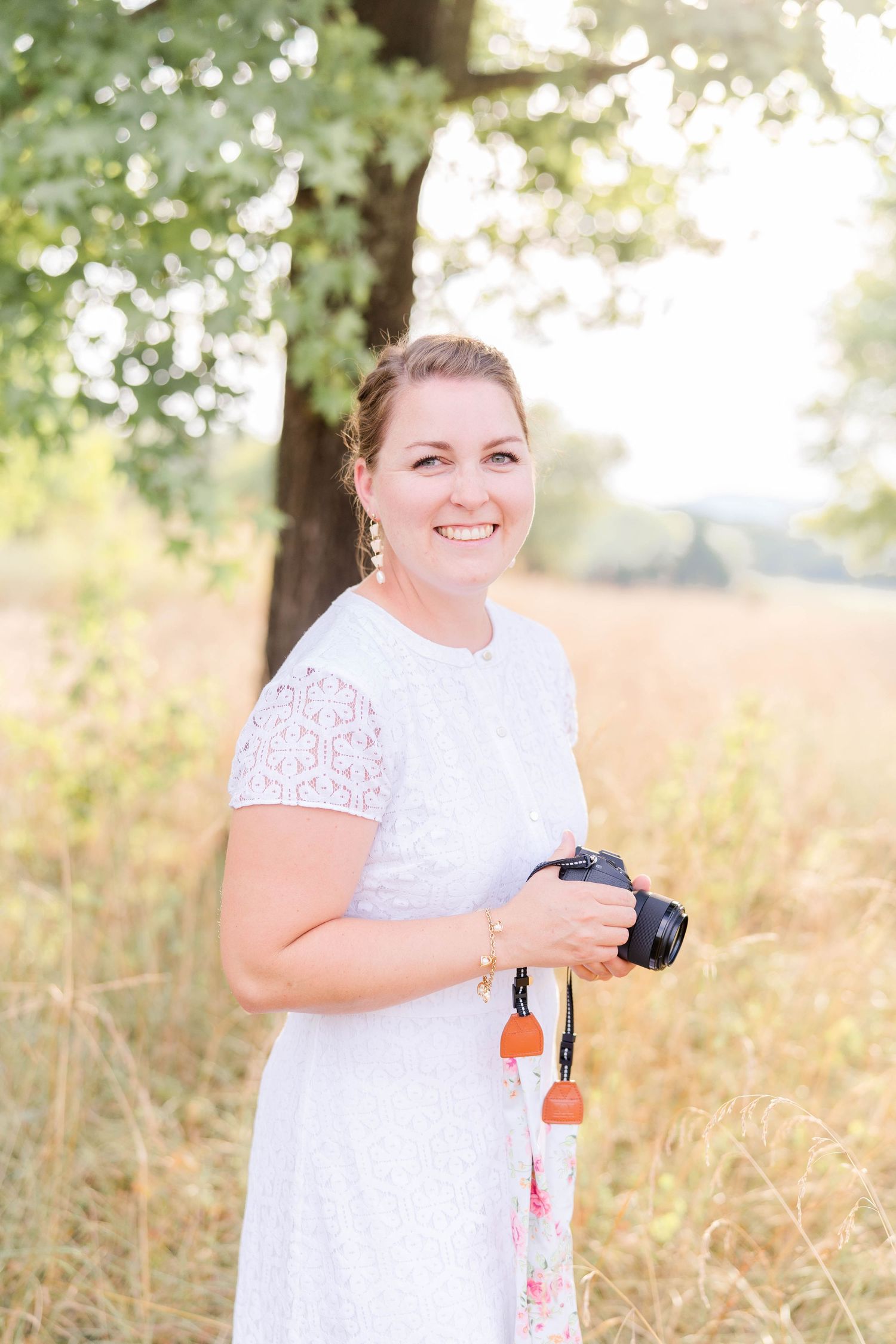 A person in a white lace dress poses outdoors in a sunlit field during a summer photo session.