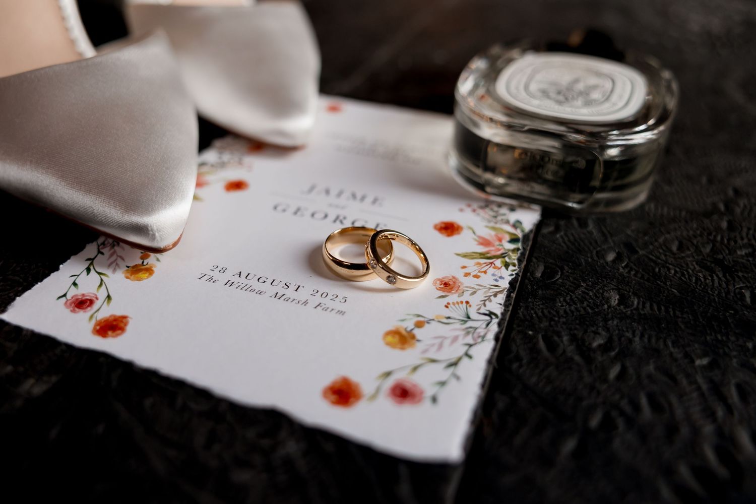 Wedding rings and invitation details artistically arranged on white paper with floral designs.