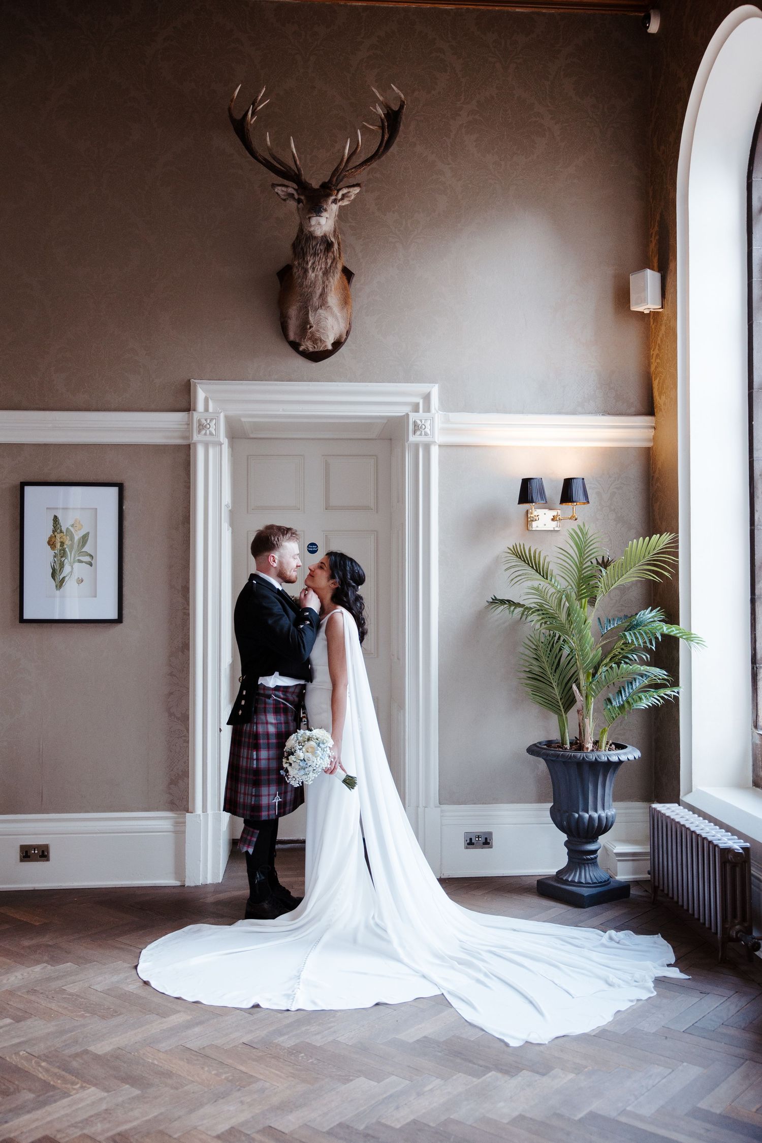 Bride and groom kissing beneath stag trophy in elegant Scottish wedding venue.