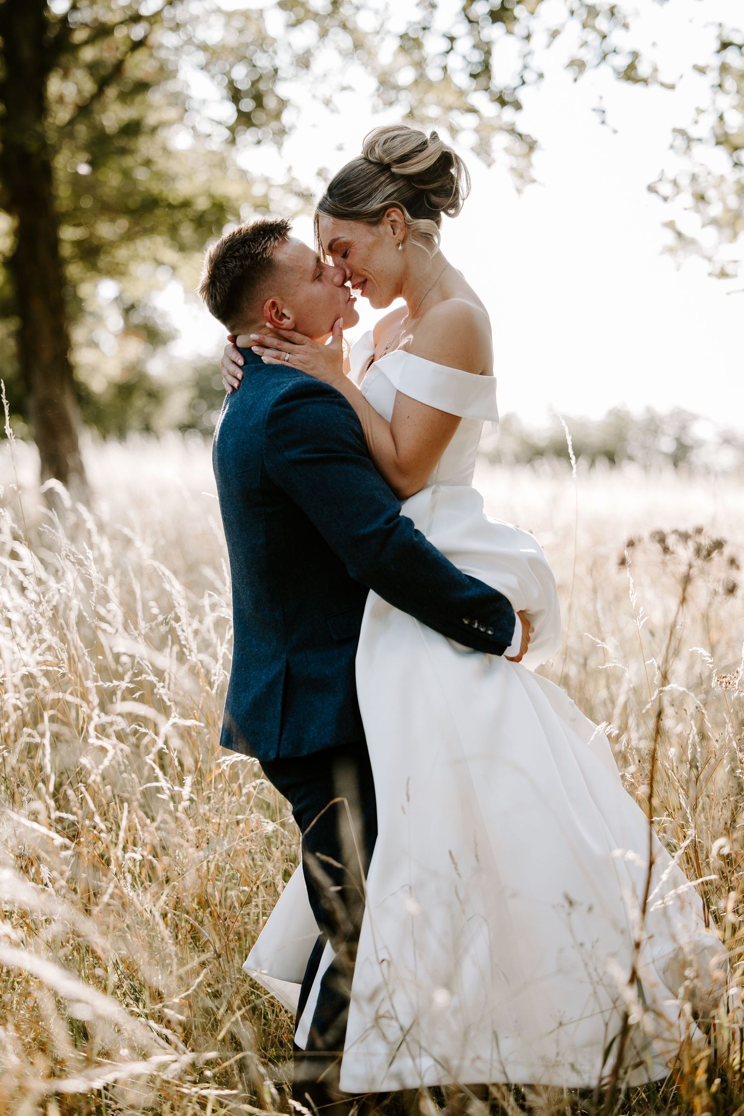 Romantic wedding couple embraces in a golden wheat field during sunset creating an intimate moment.
