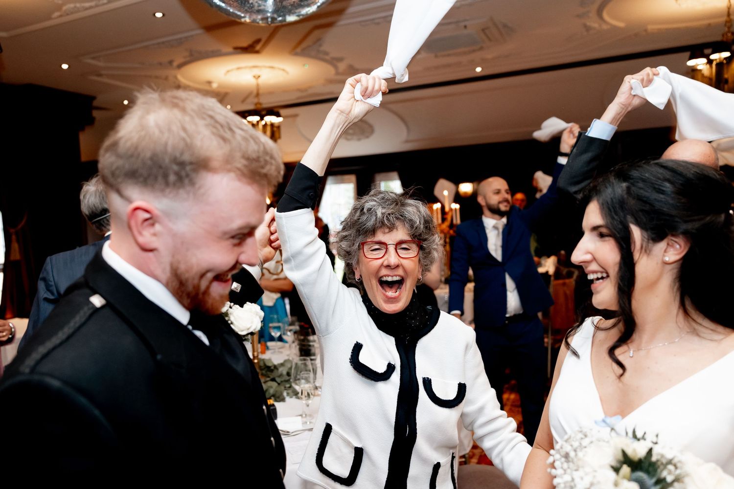 Joyful wedding celebration with bride, groom, and guest cheering at reception.