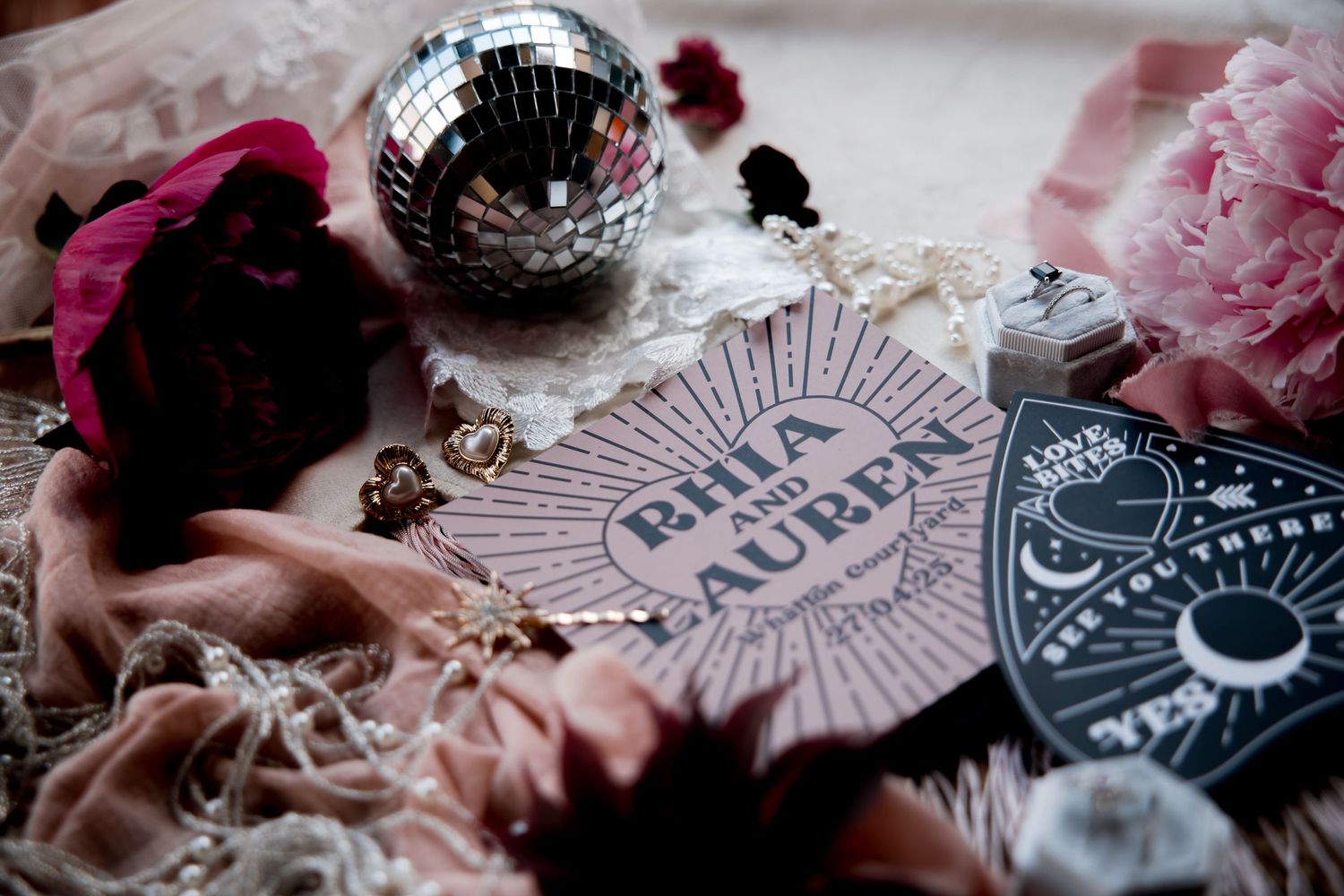 Vintage playing cards and pink flowers arranged with decorative elements and a disco ball on a dark surface.