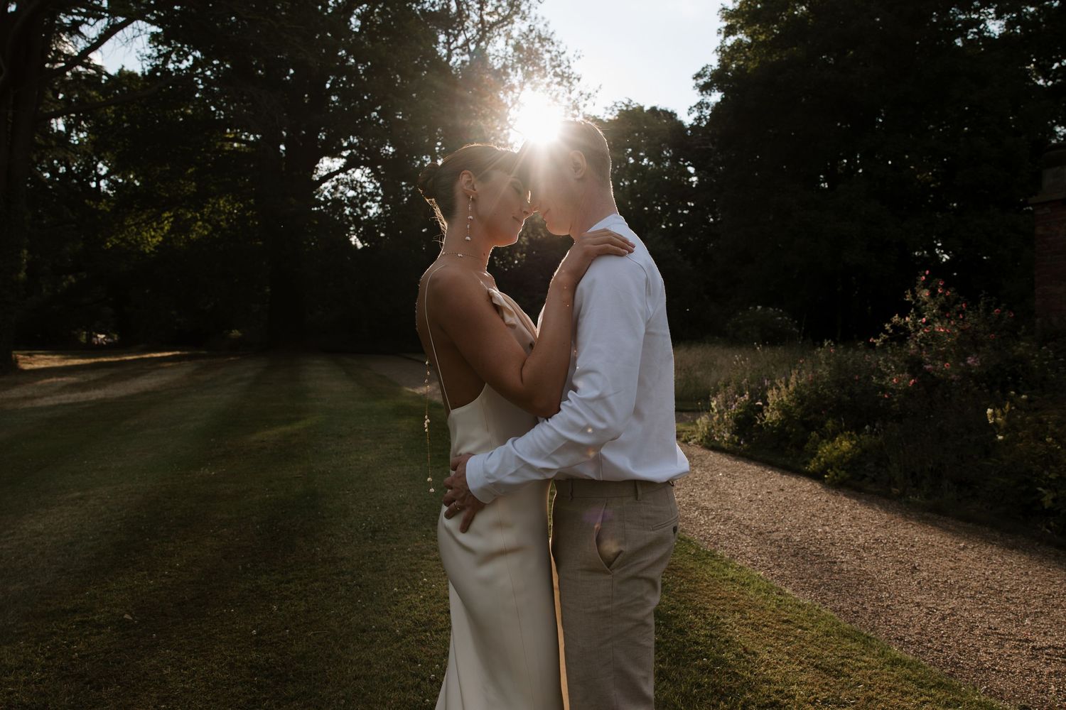 Couple embracing outdoors during golden hour with sunlight streaming through trees.