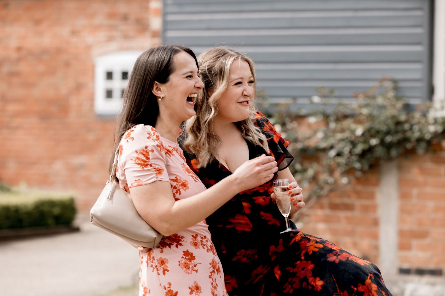 Wedding guests in floral dresses sharing joyful moments at outdoor venue.