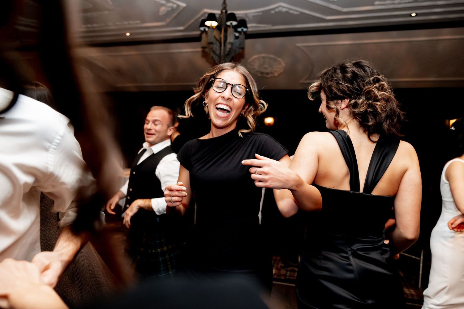 Guests laugh and dance joyfully at a lively wedding reception party in a dimly lit venue.