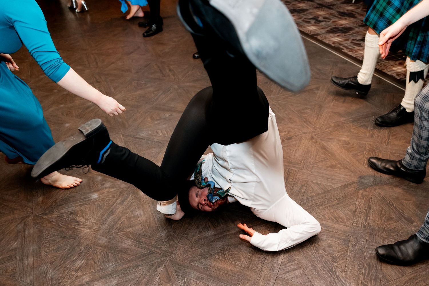 Person breakdancing on a wooden dance floor at a party, surrounded by other guests in colorful outfits.