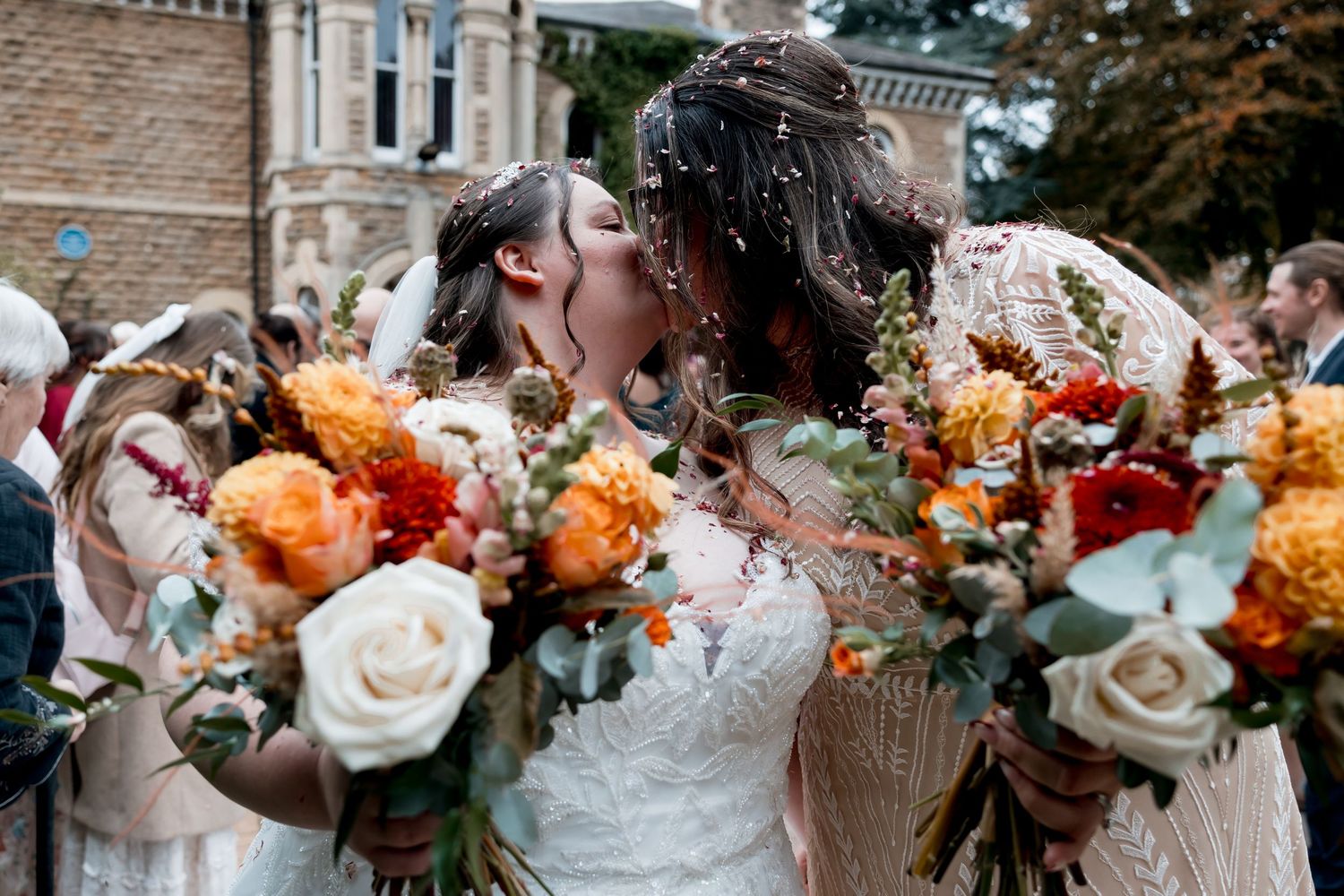 Wedding party holding vibrant orange and white floral bouquets outdoors.