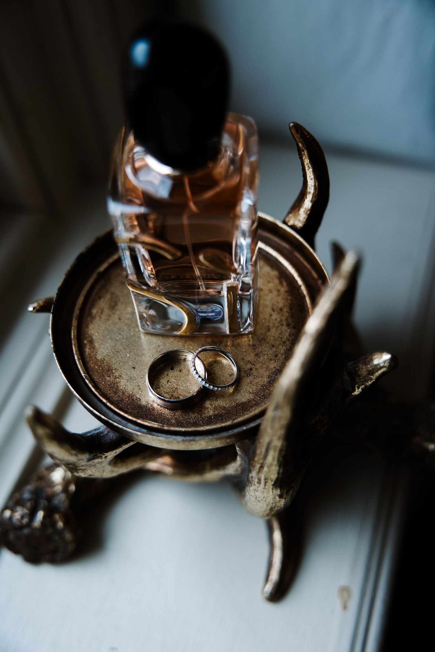 Gold antler tray with wedding rings and perfume bottle on windowsill.