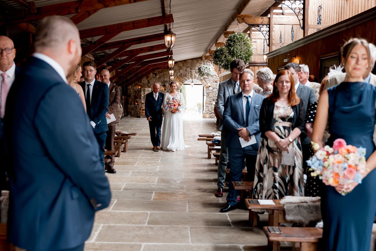 Wedding ceremony processional in rustic outdoor covered walkway.