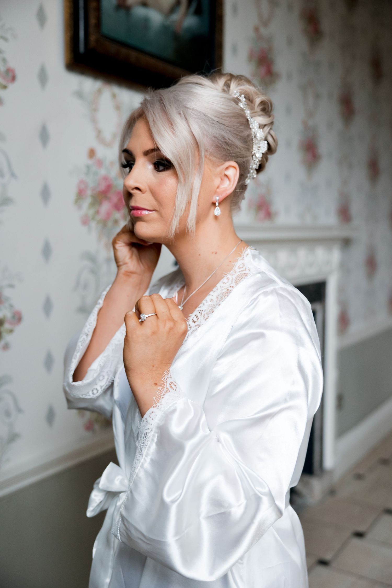 Elegant white satin robe with lace details against floral wallpaper.