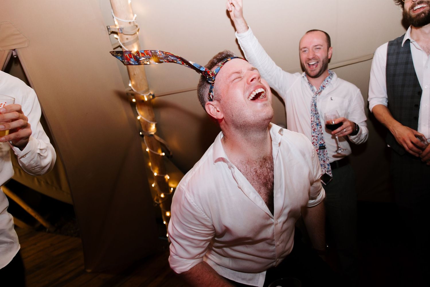 Wedding guests dancing and celebrating under warm lighting at an indoor reception.